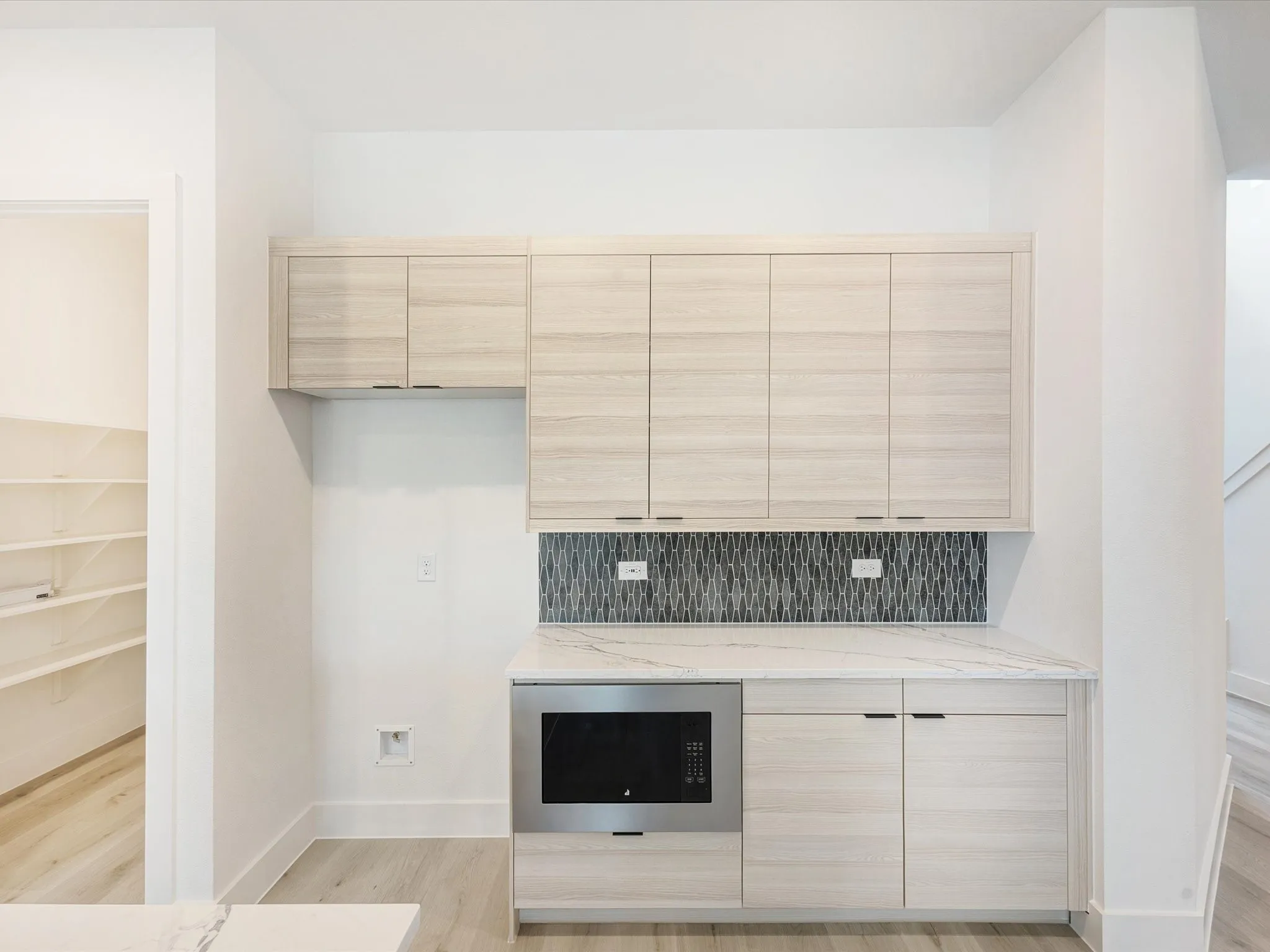 Bar area with light brown cabinets, modern cabinets, light stone countertops, light wood-style floors, and black microwave