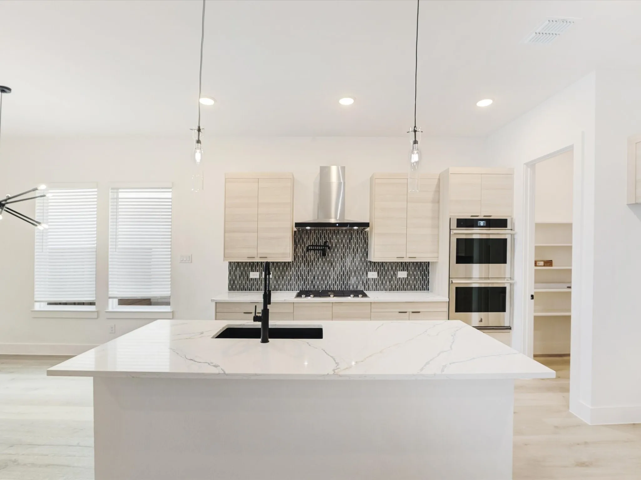 Kitchen with backsplash, light stone counters, hanging light fixtures, light brown cabinets, and light wood finished floors