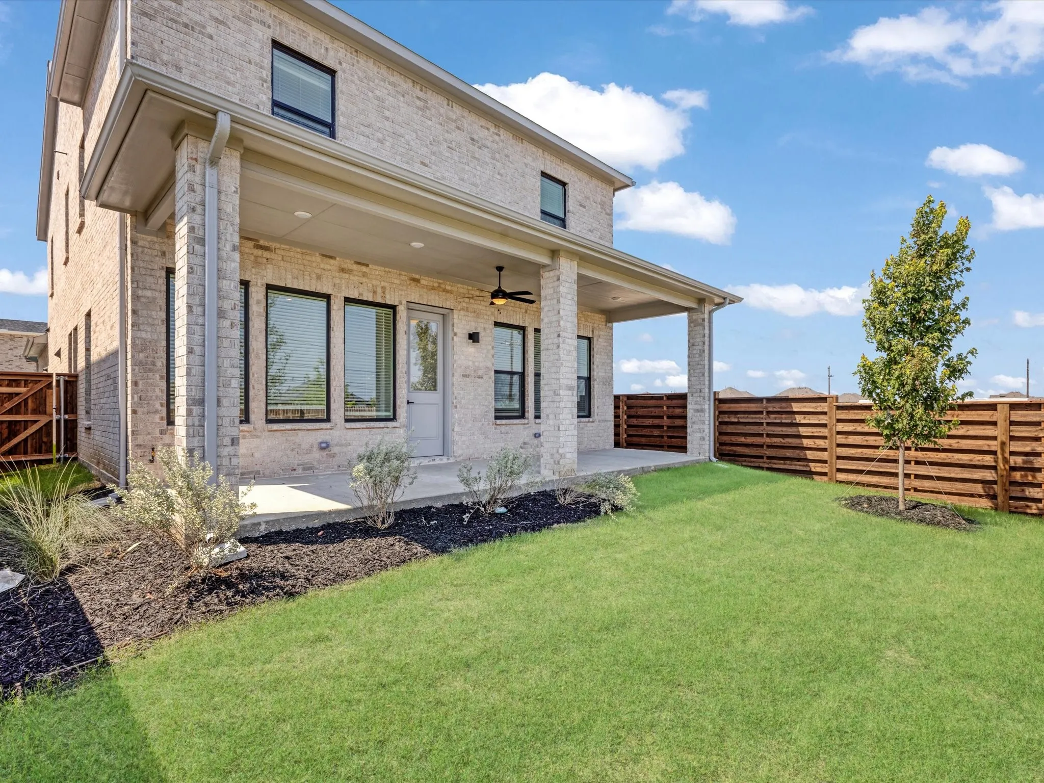 Rear view of house with brick siding, a fenced backyard, a ceiling fan, and a patio area