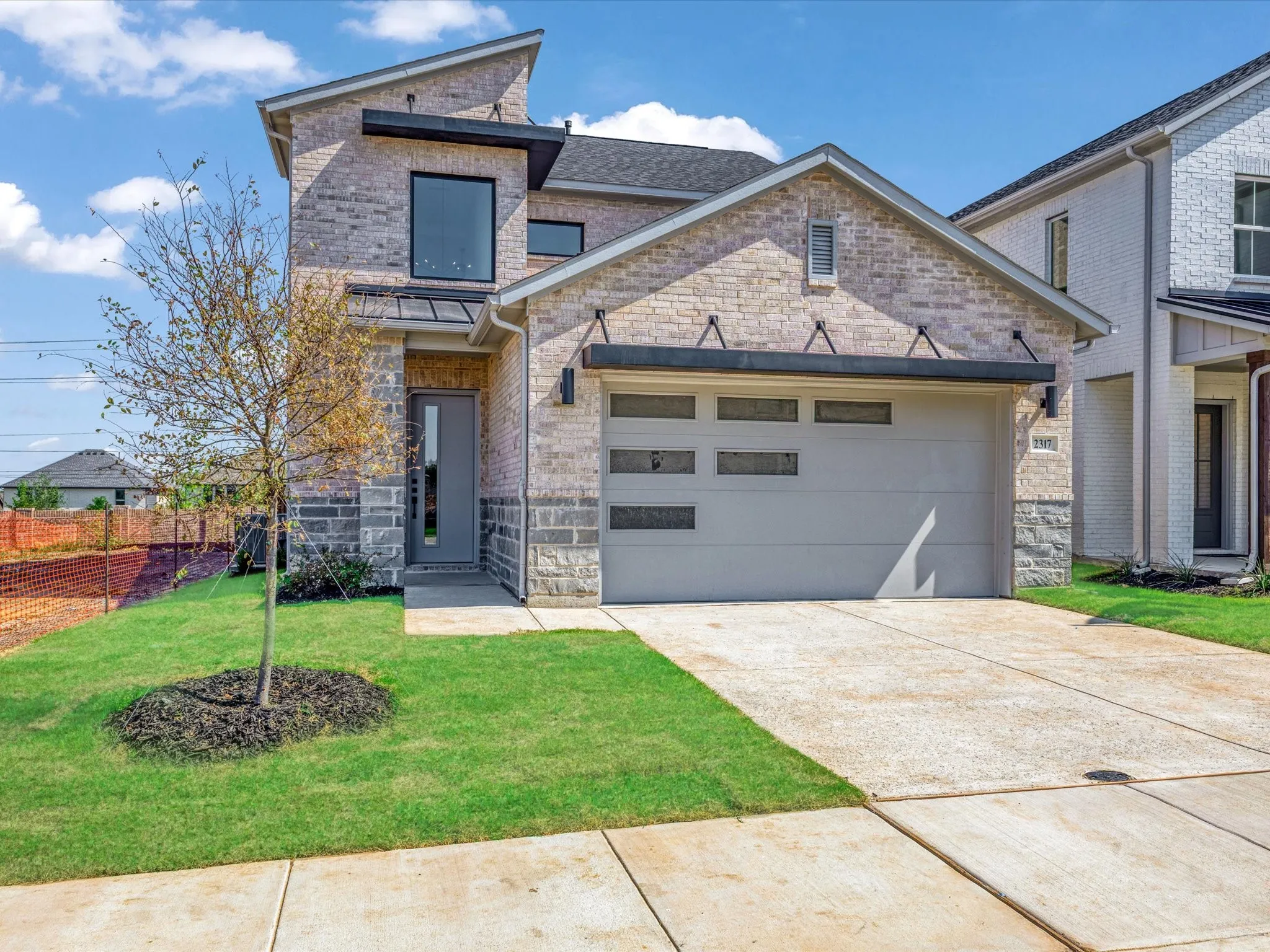 View of front of property featuring brick siding, a garage, concrete driveway, and stone siding