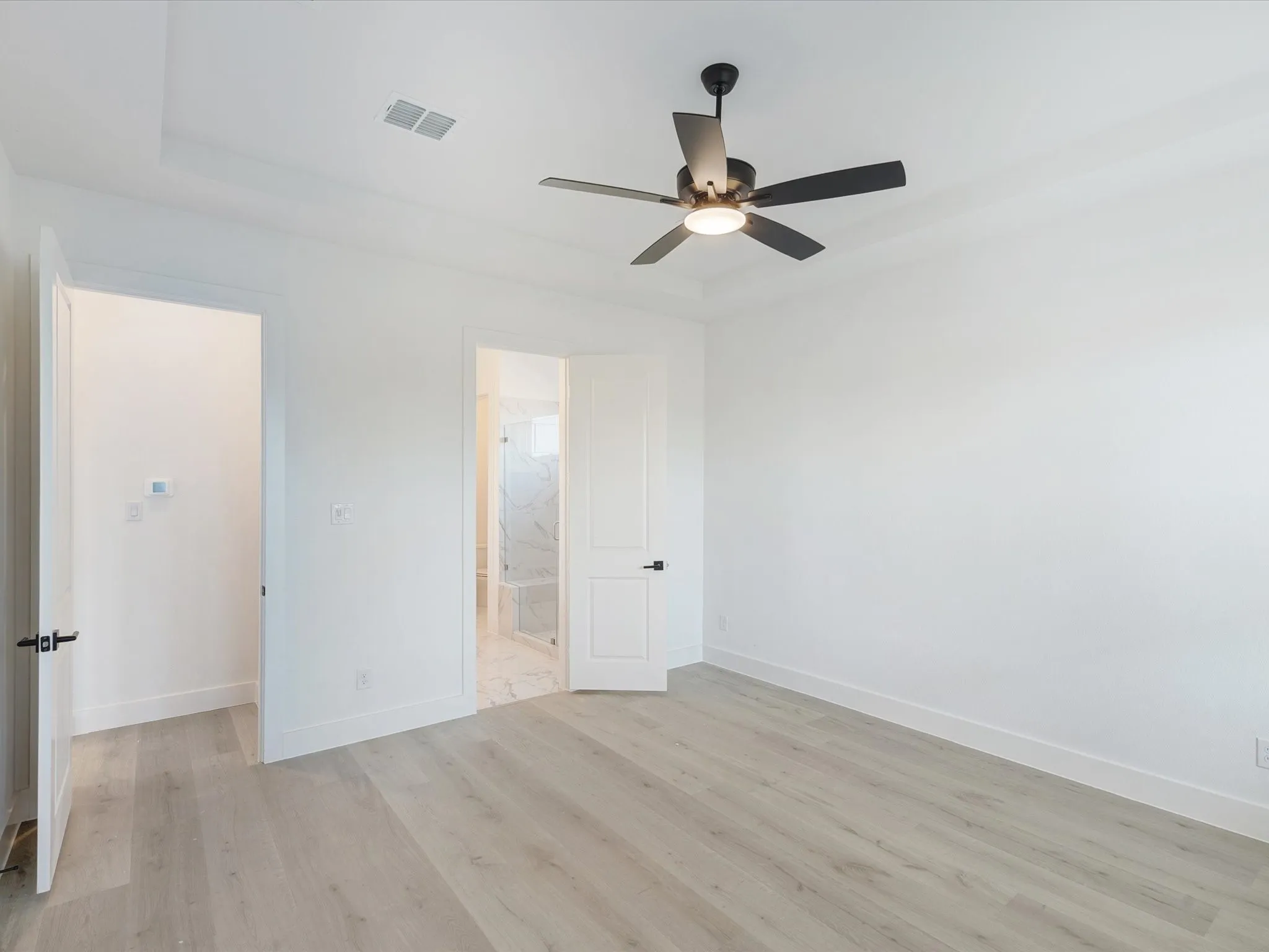 Primary bedroom featuring light wood-style floors, ceiling fan, and ensuite bath