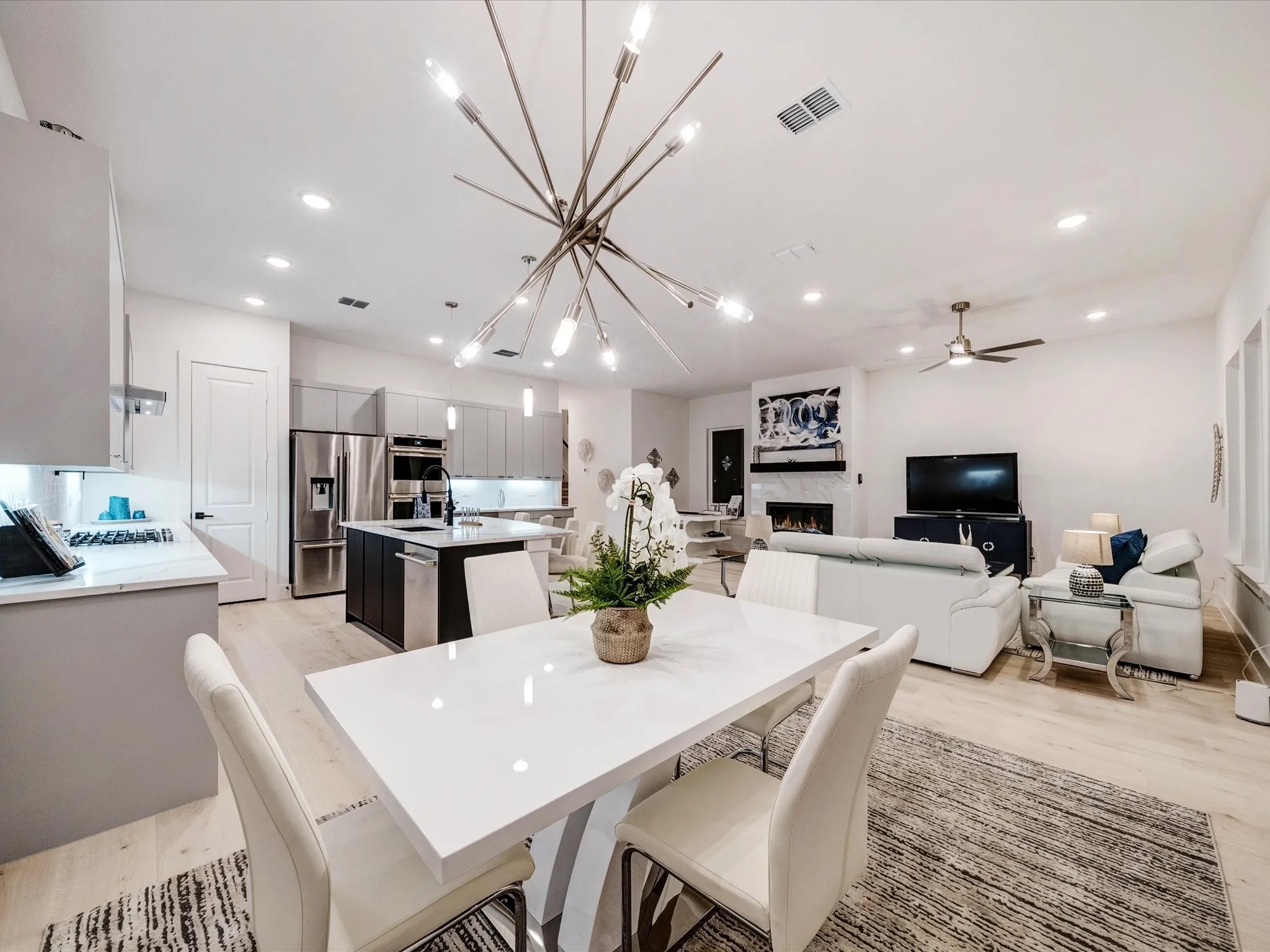 Dining space with a chandelier, light wood-style floors, a warm lit fireplace, recessed lighting, and a ceiling fan