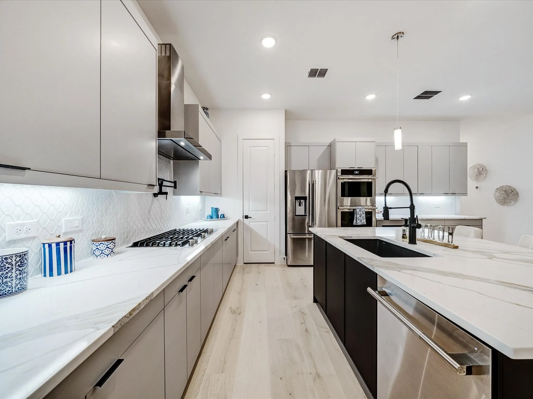 Kitchen with modern cabinets, appliances with stainless steel finishes, light stone countertops, hanging light fixtures, and recessed lighting