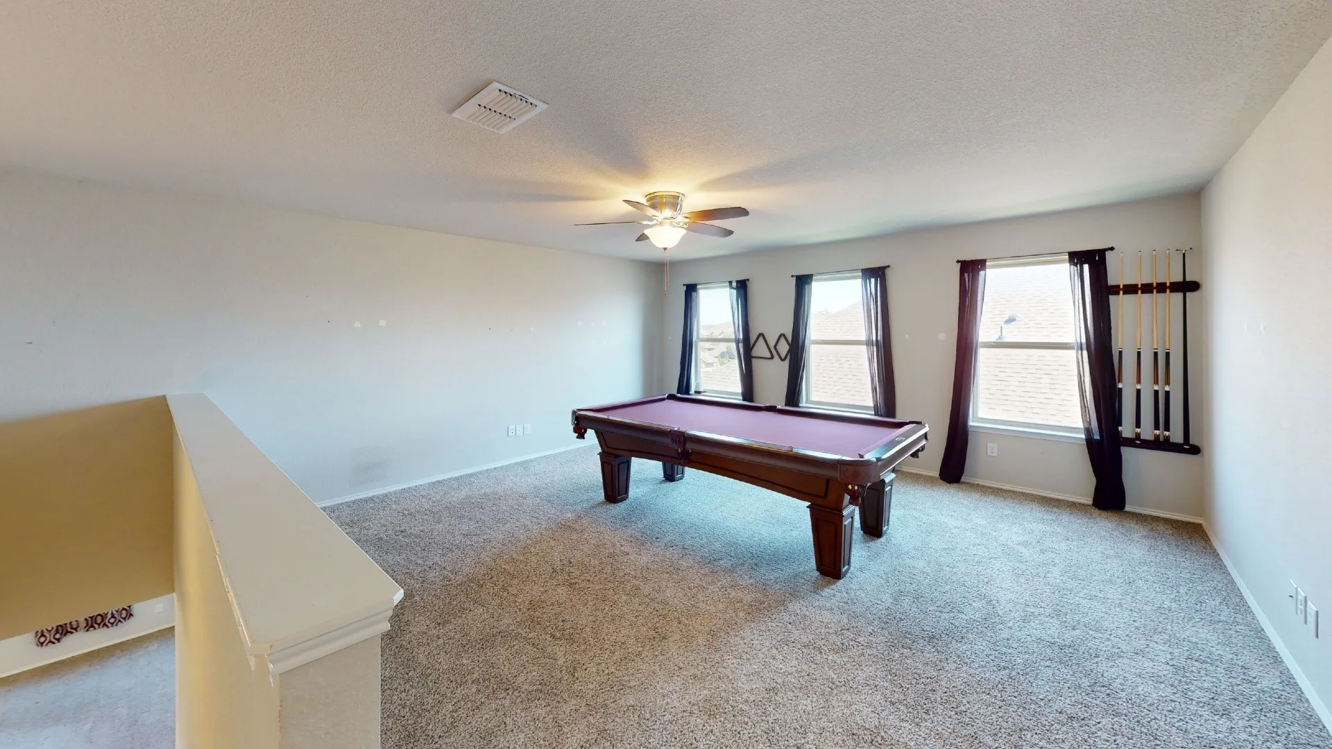 Spacious room with light-colored carpeting, multiple windows, and a ceiling fan with integrated lighting