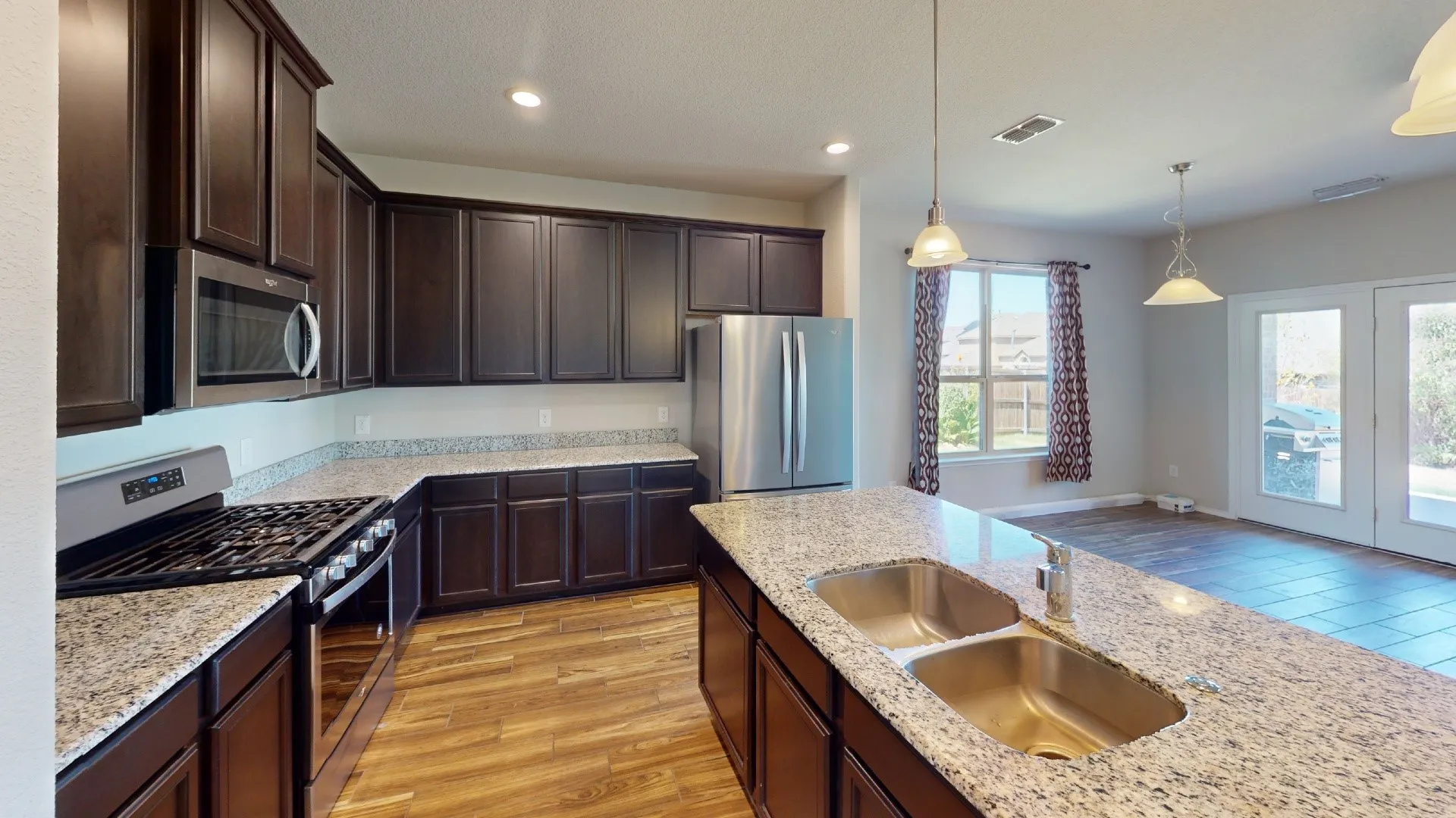 Kitchen featuring abundant dark wood cabinetry, light-colored speckled countertops, stainless steel appliances, and wood-finish flooring
