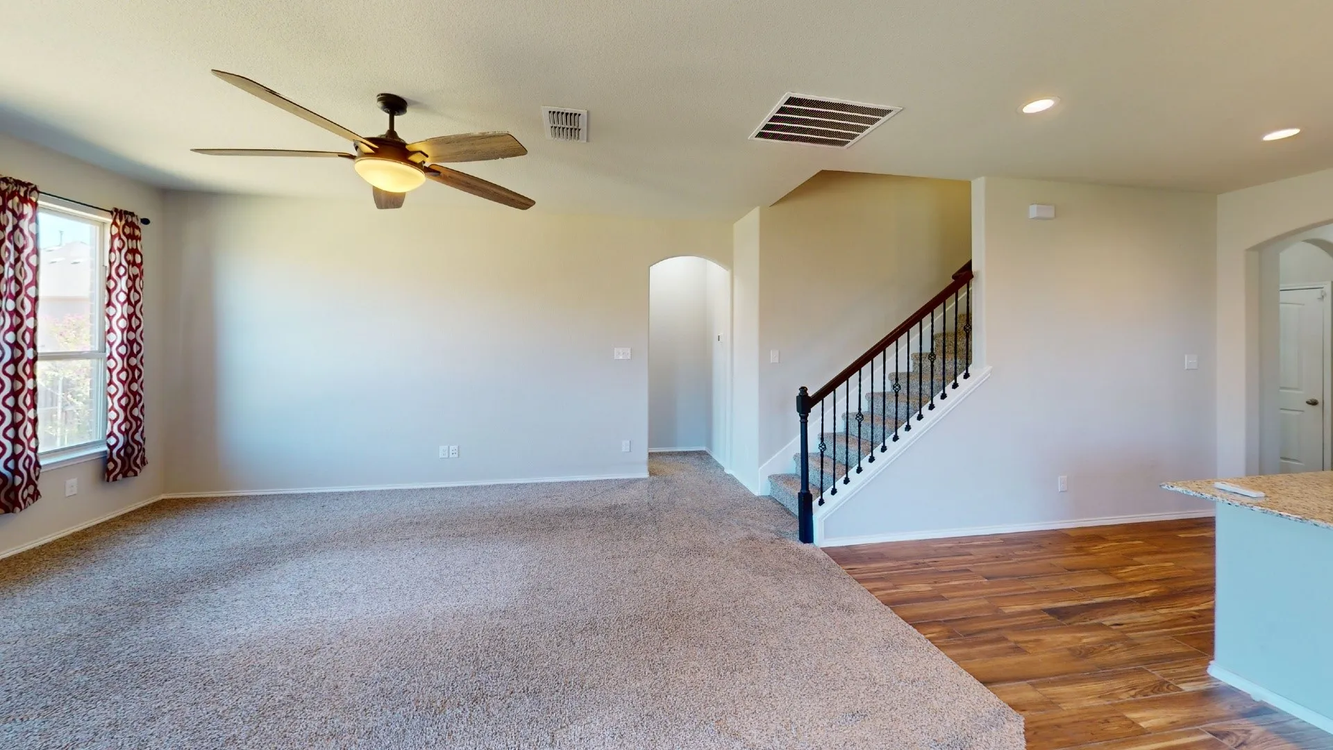 Spacious open-concept living area featuring neutral paint finishes, ceiling fan with integrated lighting, and wood-finish flooring