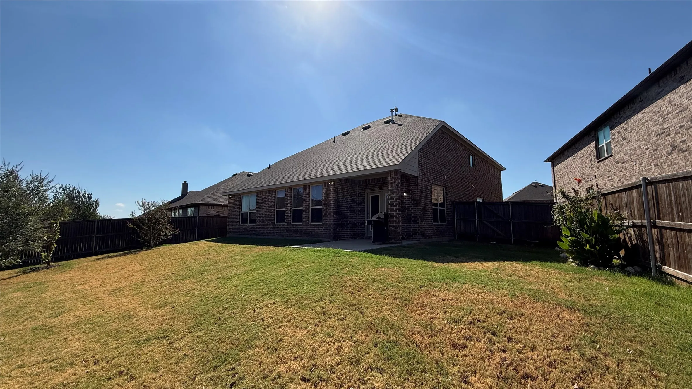 Expansive backyard featuring a manicured lawn, full brick exterior, a covered patio, and privacy fencing