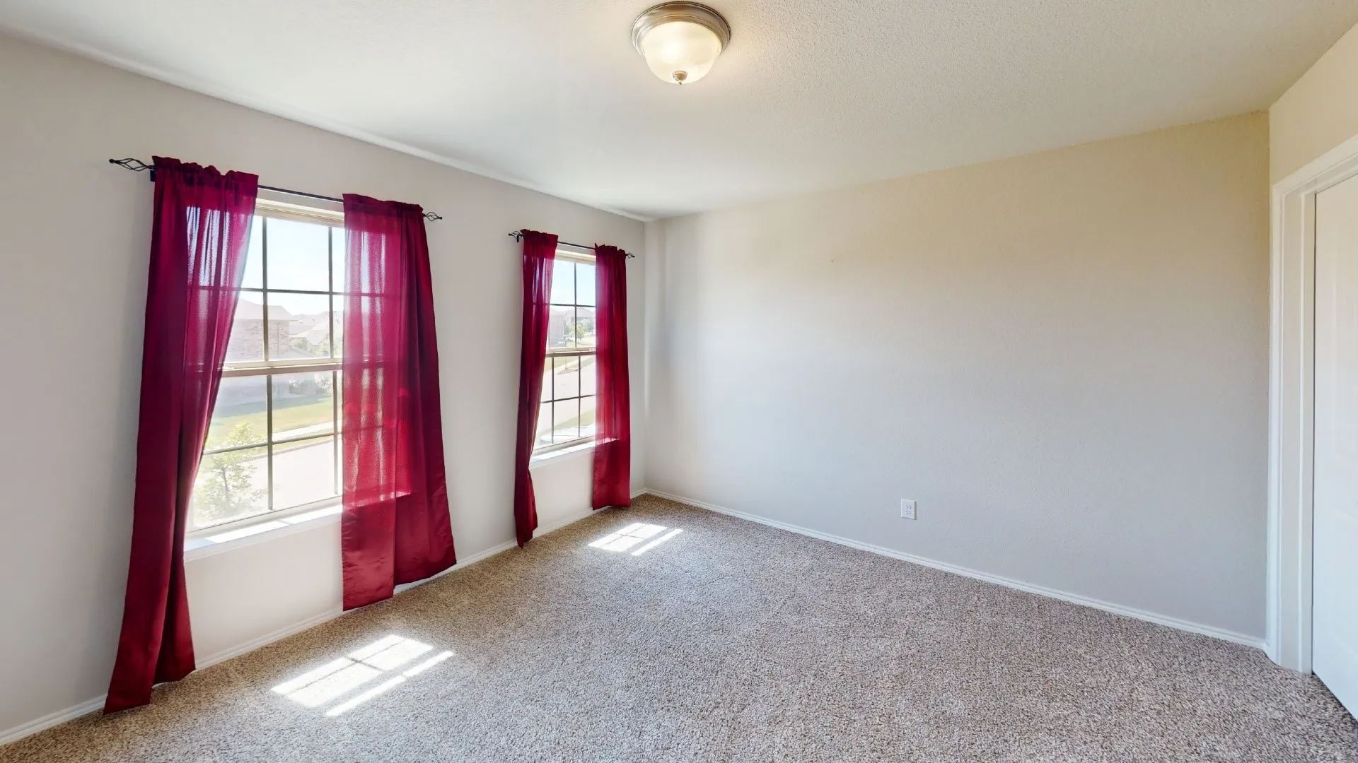 Wall-to-wall carpeting with light-toned walls, featuring two grid-pattern windows, and a flush mount ceiling light fixture
