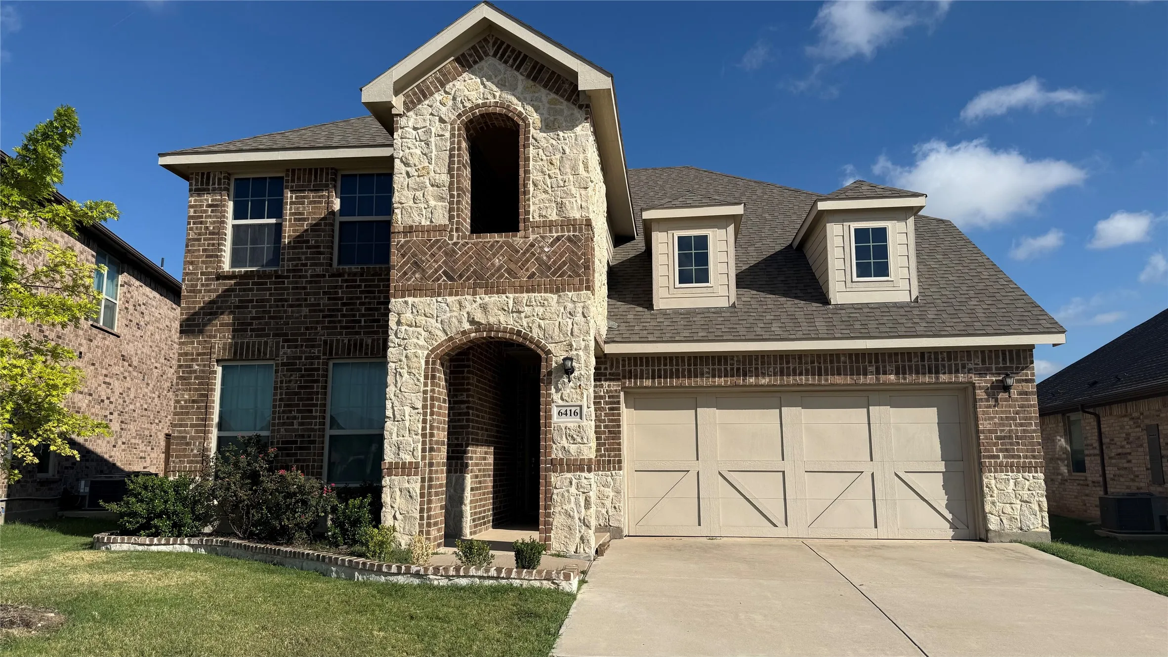Two-story exterior with brick and stone accents, an arched entry, a two-car garage, and dormer windows