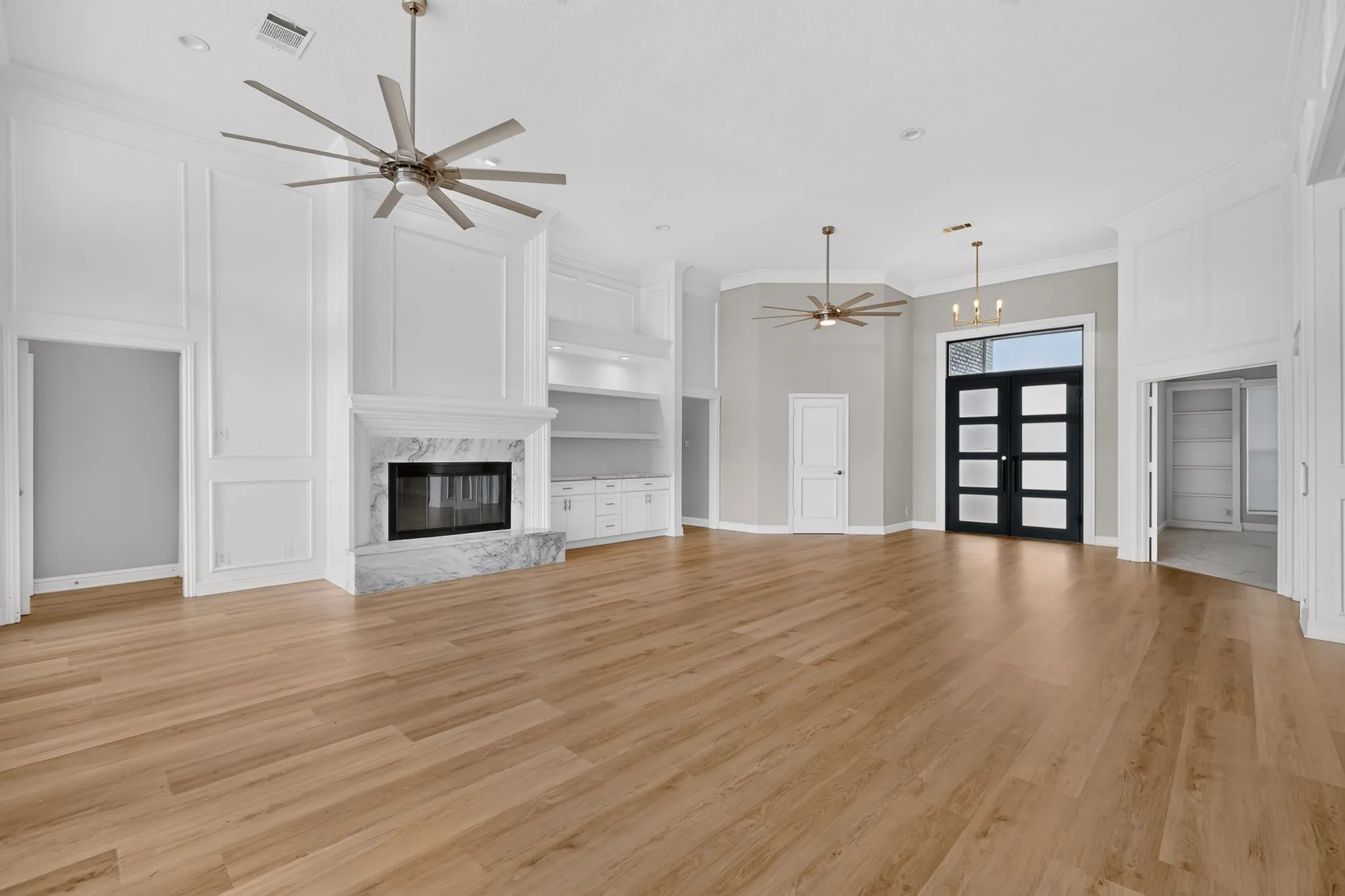 Expansive living space featuring wood-finish flooring, a contemporary fireplace with stone surround, custom built-in cabinetry, and a modern double-door entry