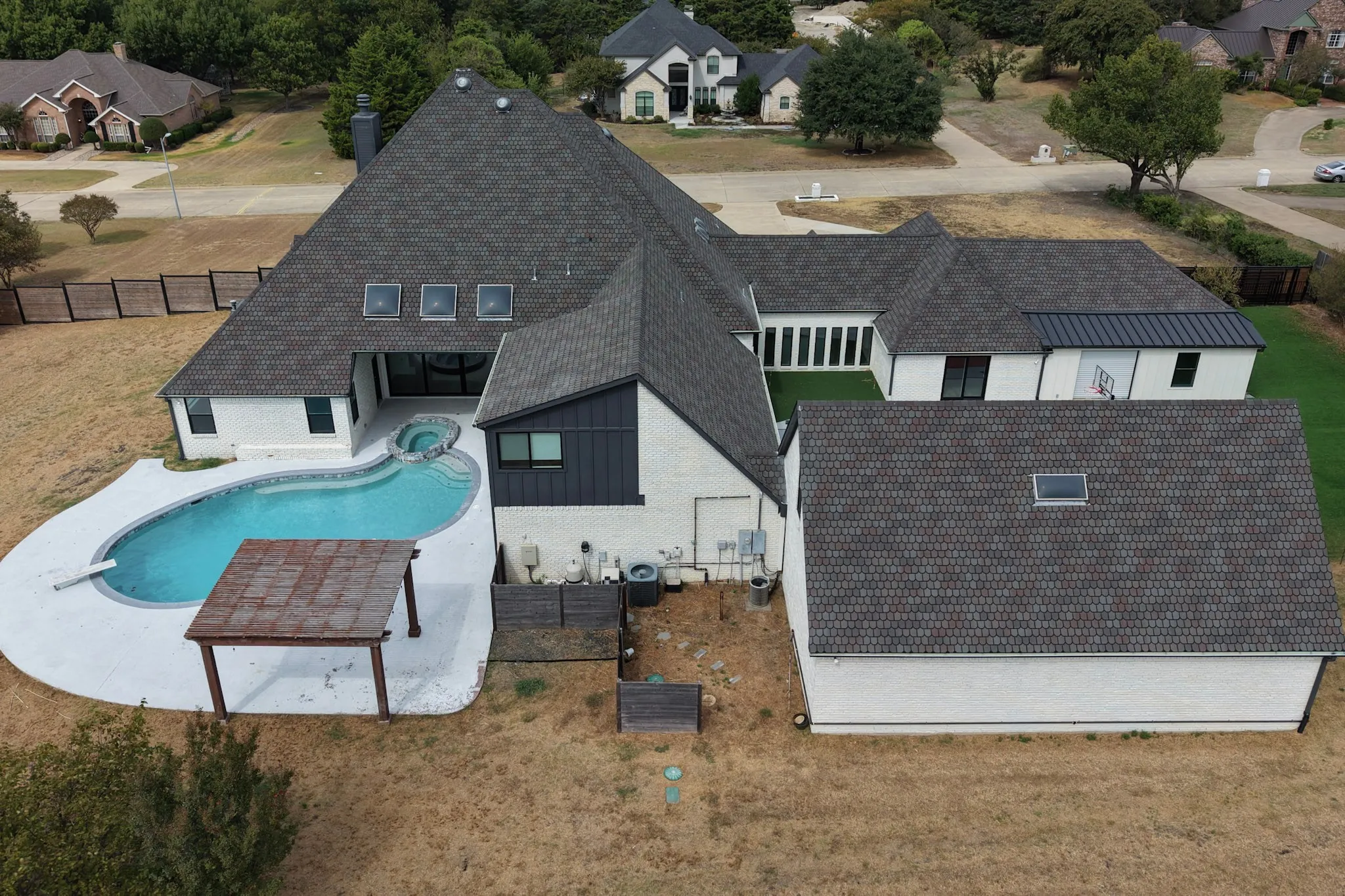 Curved swimming pool with an integrated spa, expansive patio, and a detached pergola structure