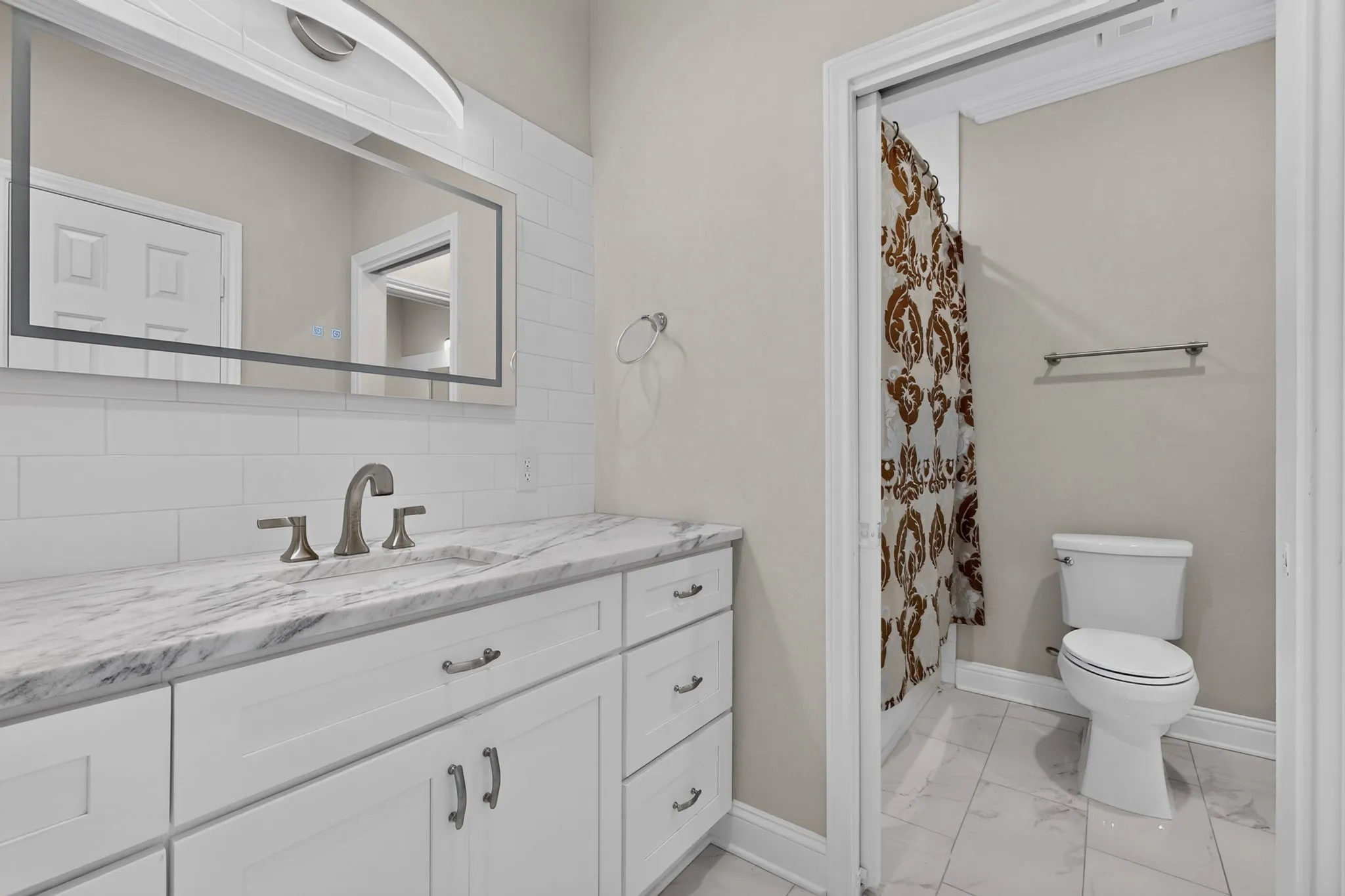 White subway tile backsplash, integrated sink with brushed nickel faucet, large vanity mirror with integrated lighting, and white cabinet vanity with drawer and cabinet storage