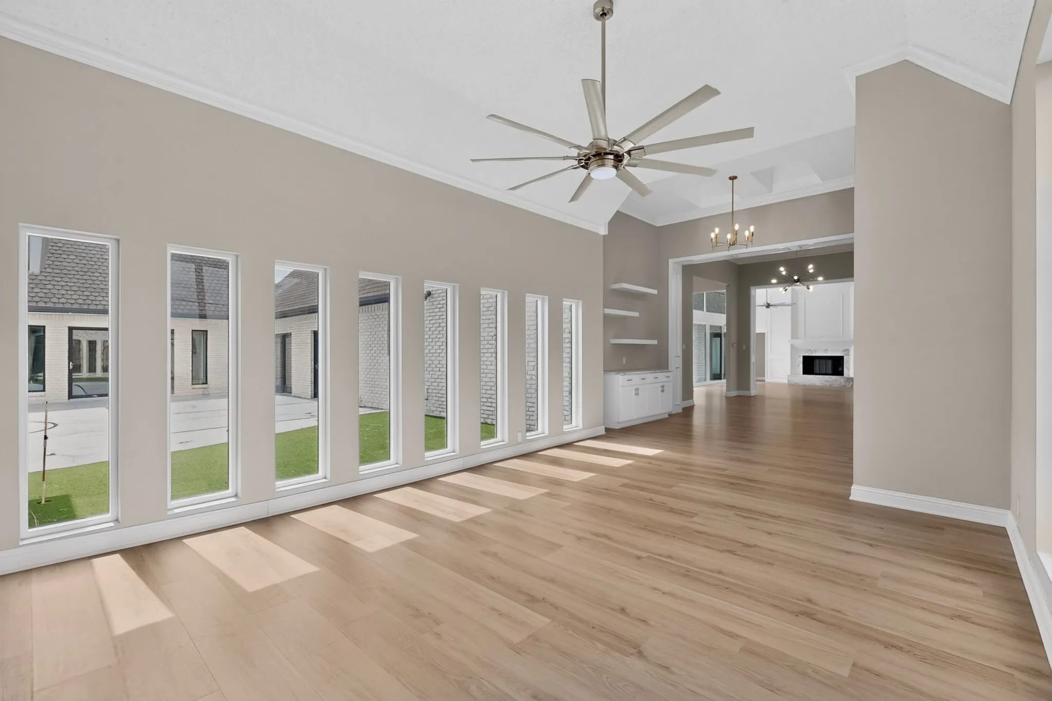 Vaulted ceiling with a contemporary ceiling fan, wood-finish flooring, custom built-in cabinetry with floating shelves, and multiple vertical windows