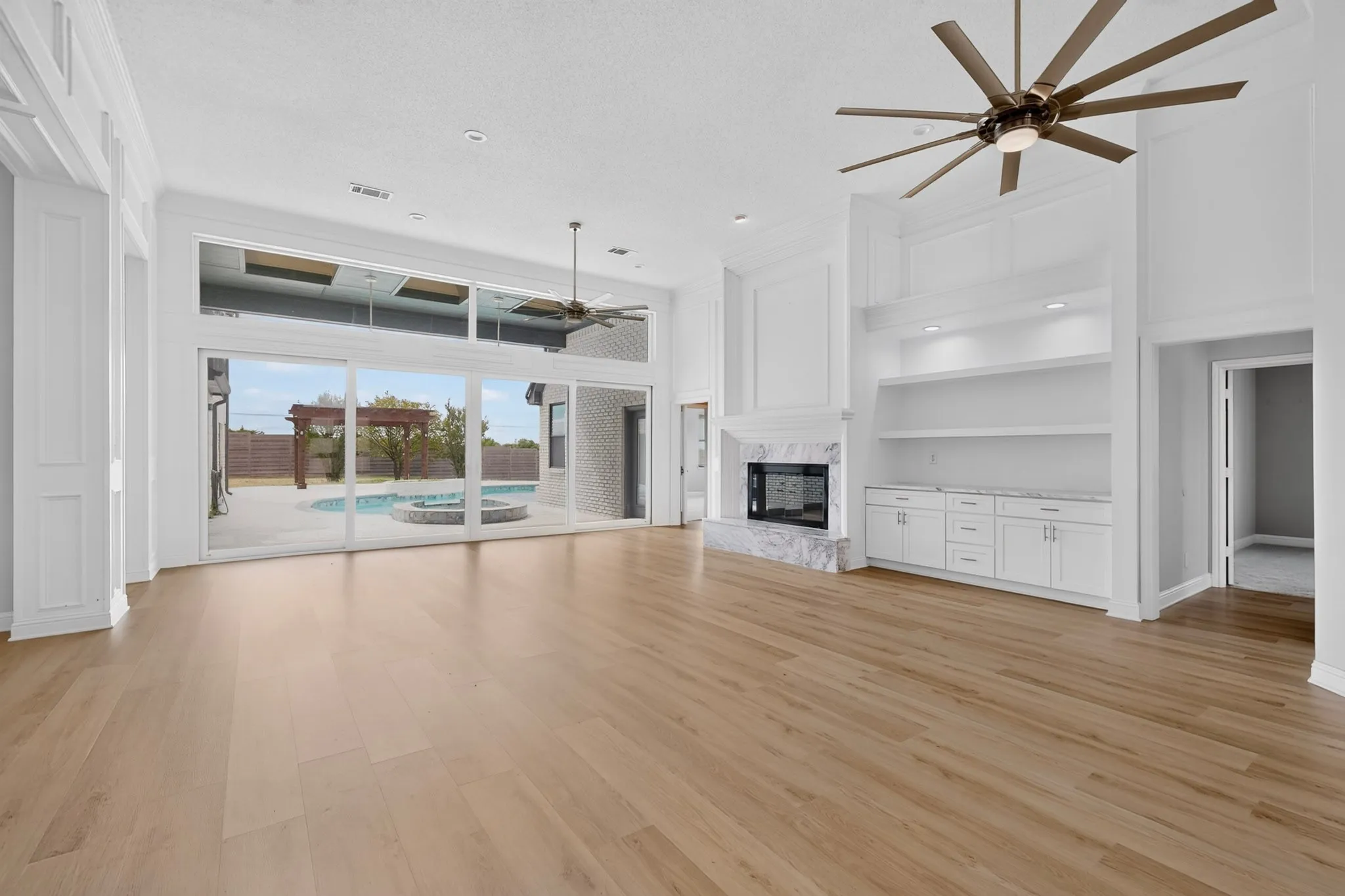 Wood-finish flooring, built-in entertainment center, marble-surround fireplace, large ceiling fan, and sliding glass doors to a backyard pool