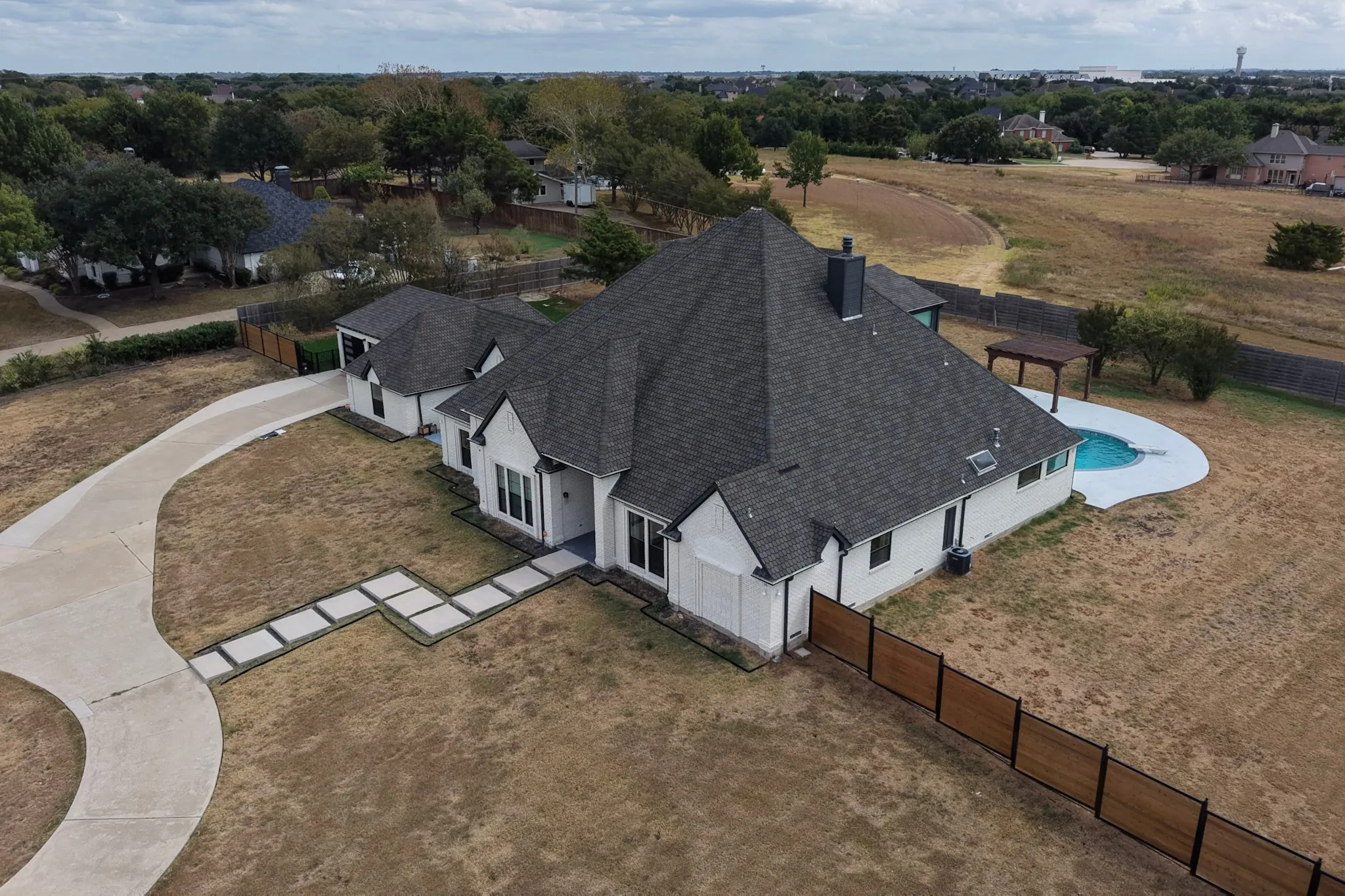 Expansive residence with a dark shingle roof, a curving concrete driveway, and a backyard swimming pool