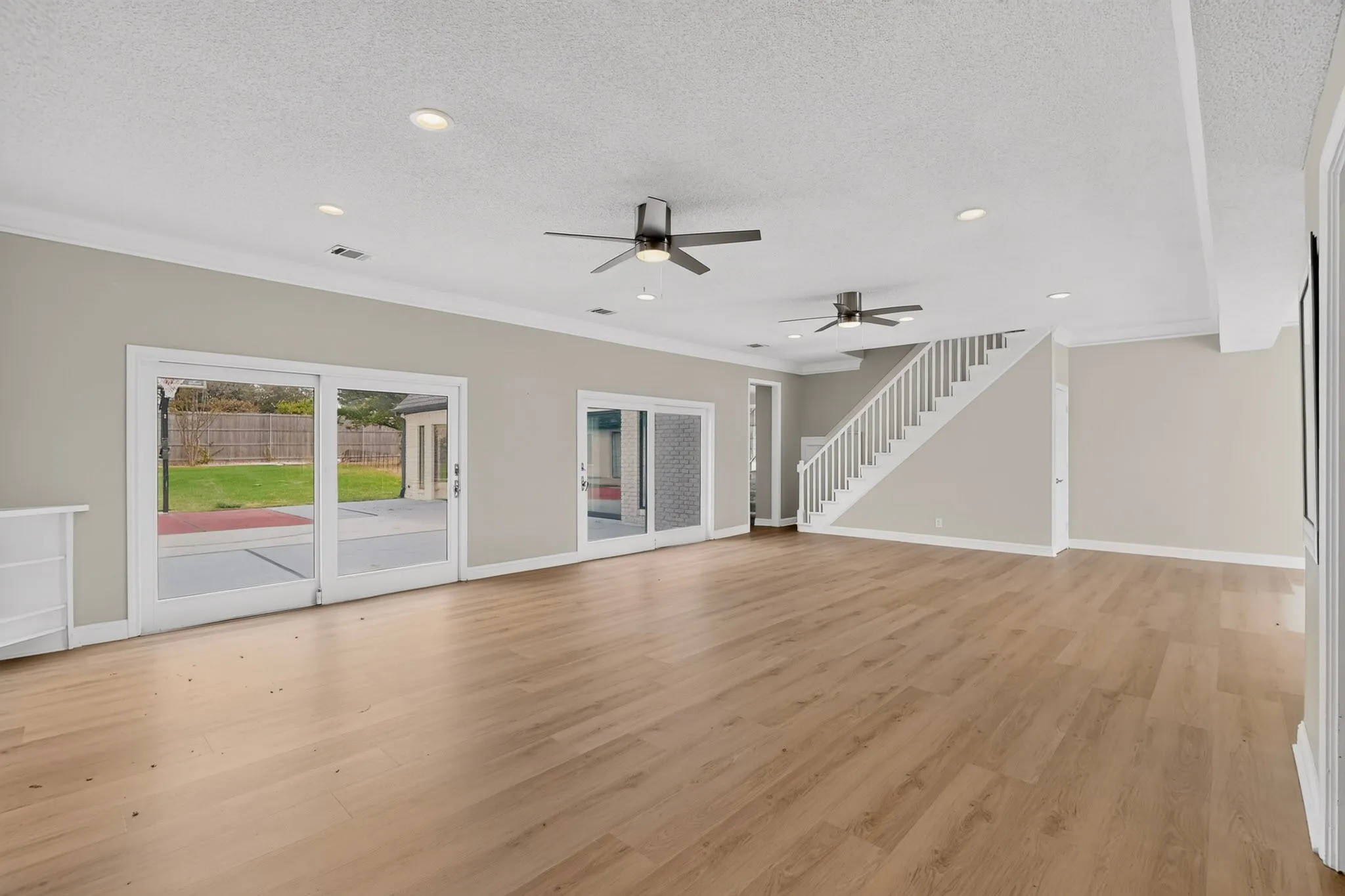 Expansive open-concept room featuring wood-finish flooring, two ceiling fans, recessed lighting, and multiple sliding glass doors to the exterior