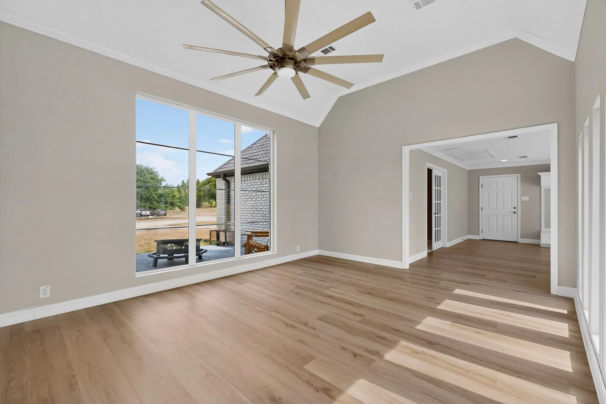 Vaulted ceiling, ceiling fan with integrated lighting, wood-finish flooring, large multi-pane window, cased doorway