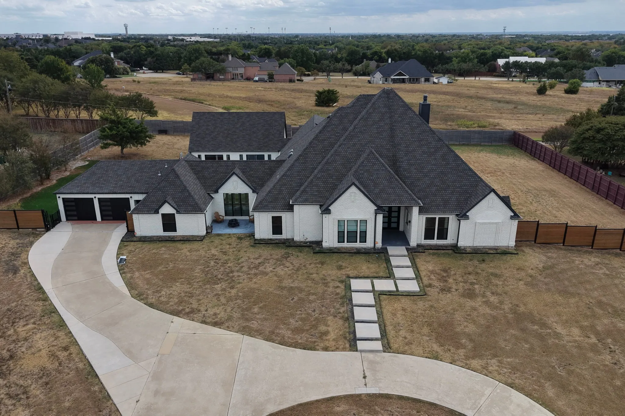 Modern farmhouse-style residence with a dark shingle roof, white exterior, and a multi-section privacy fence