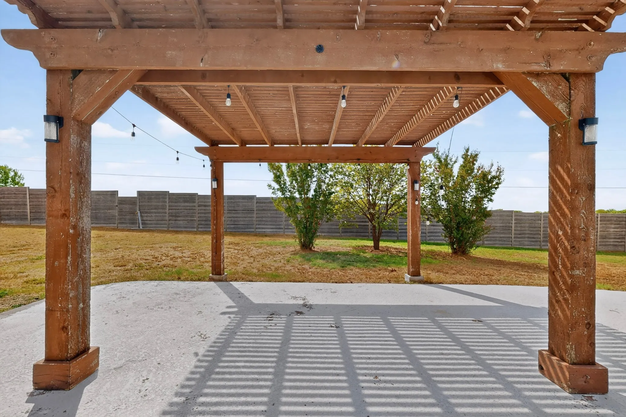 Wood pergola with string lighting over a concrete patio