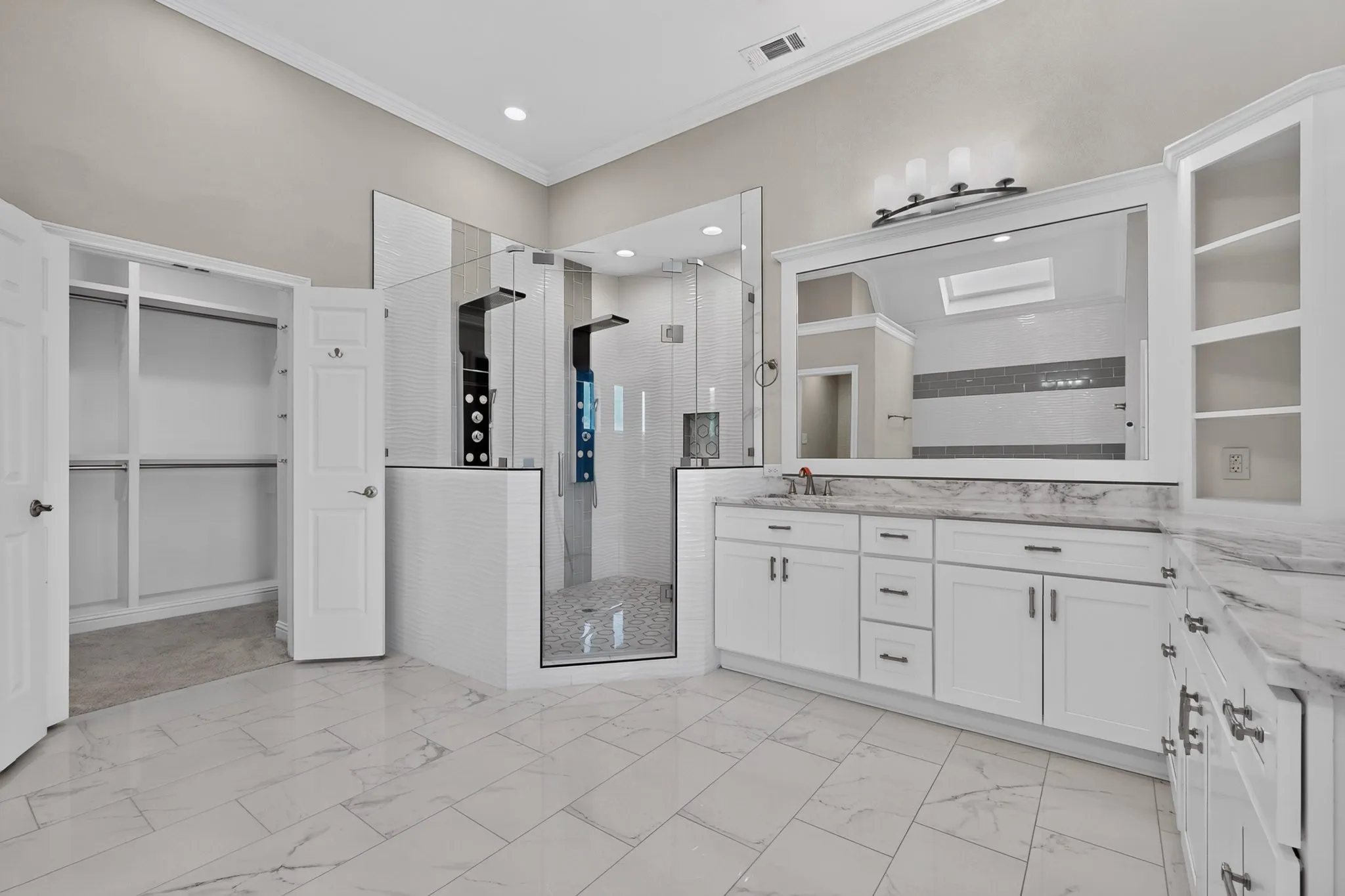 Contemporary bathroom featuring large format tile flooring, a spacious walk-in shower with dual shower panels, a double vanity with white cabinetry, and extensive built-in storage