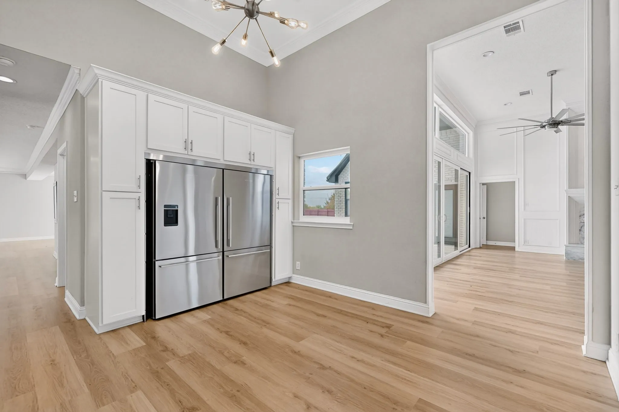 Vaulted ceilings, wood-finish flooring, white cabinetry, stainless steel refrigerator, and modern chandelier