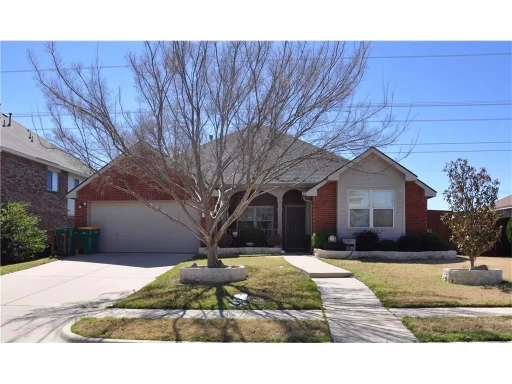 Brick single-story home in The Highlands featuring great curb appeal, a spacious front-entry garage, and a charming covered front porch perfect for relaxing.