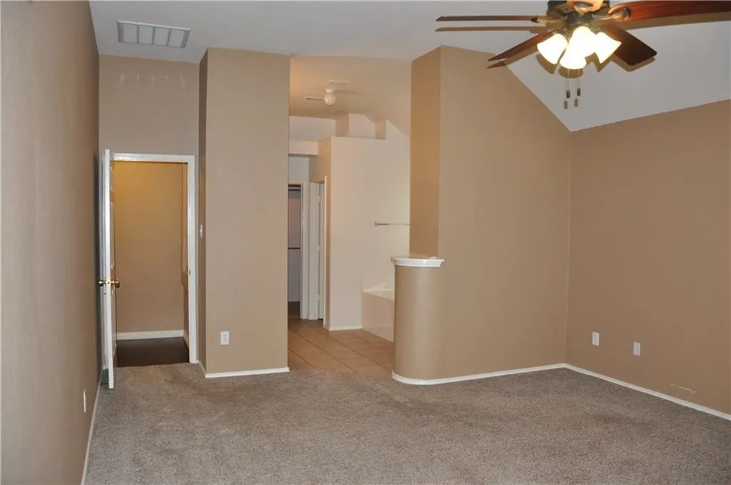 Spacious primary bedroom retreat featuring vaulted ceilings, a ceiling fan, and an en-suite layout