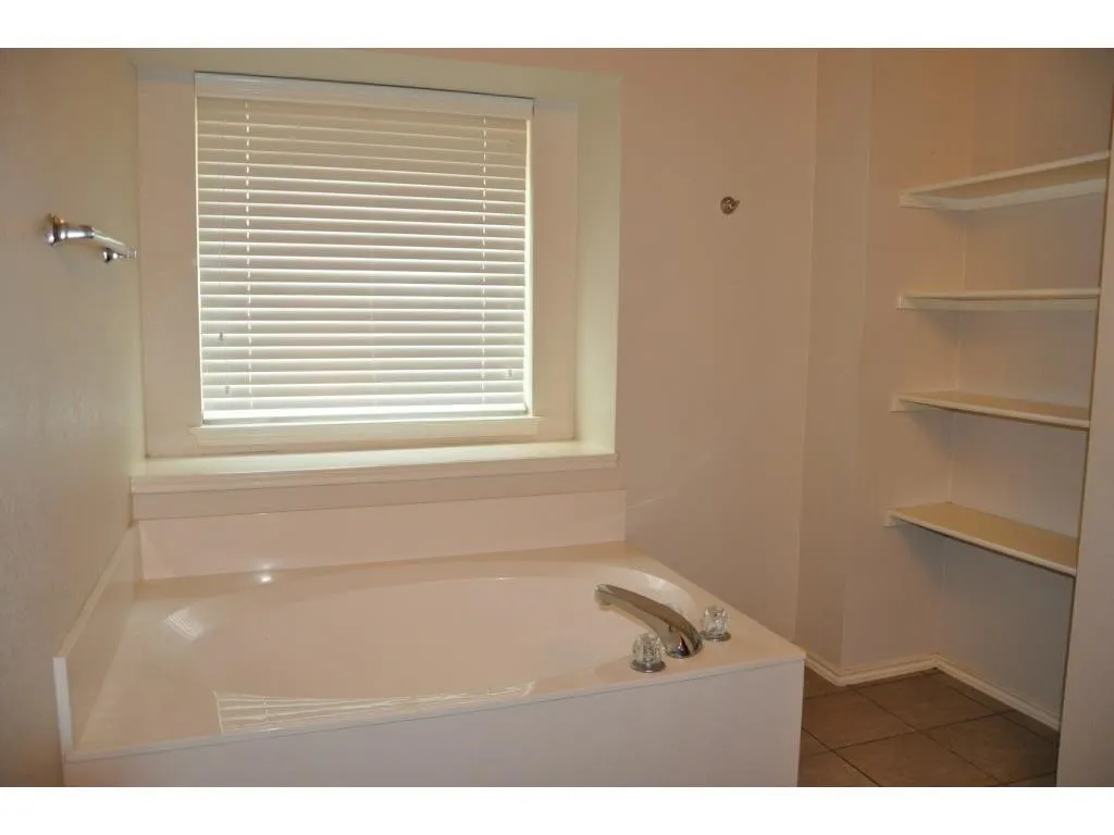 Unwind in the primary suite’s deep garden tub, complete with built-in storage shelving and privacy blinds