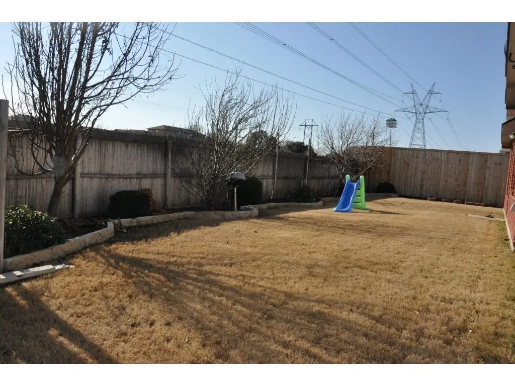 Expansive backyard featuring a natural grass lawn, wood plank fencing, and mature trees