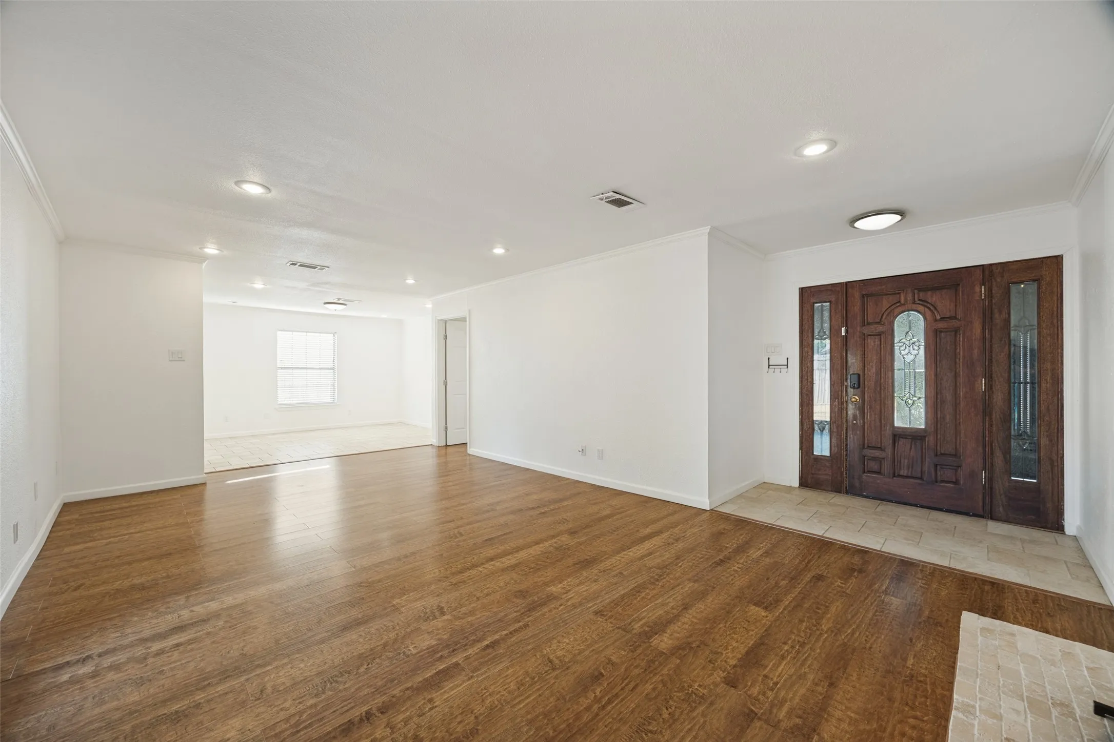 Hardwood flooring throughout, recessed lighting, and a detailed wood entry door with decorative glass side panels