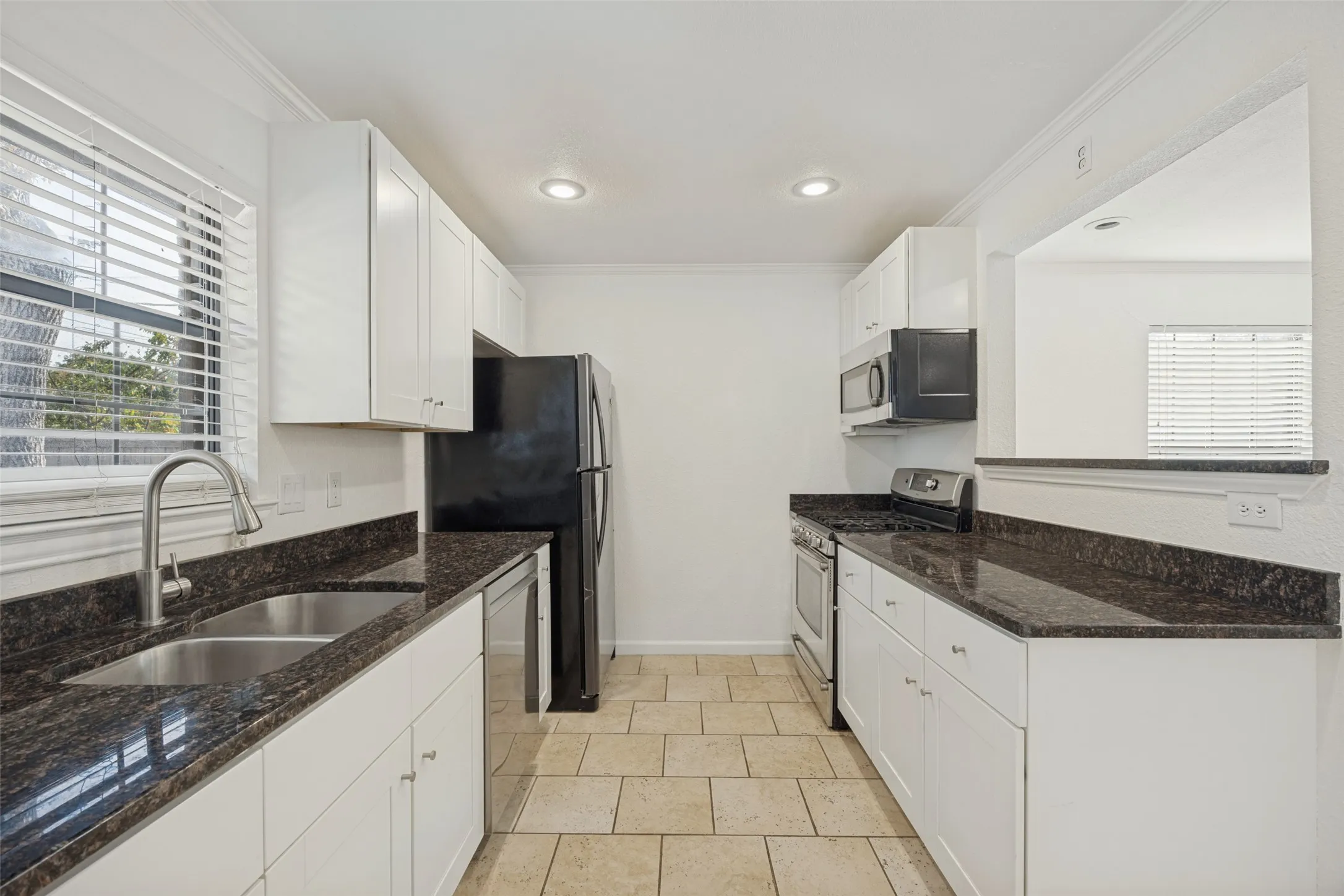 Galley kitchen with white cabinetry, dark stone countertops, stainless steel sink, tile flooring, and recessed lighting