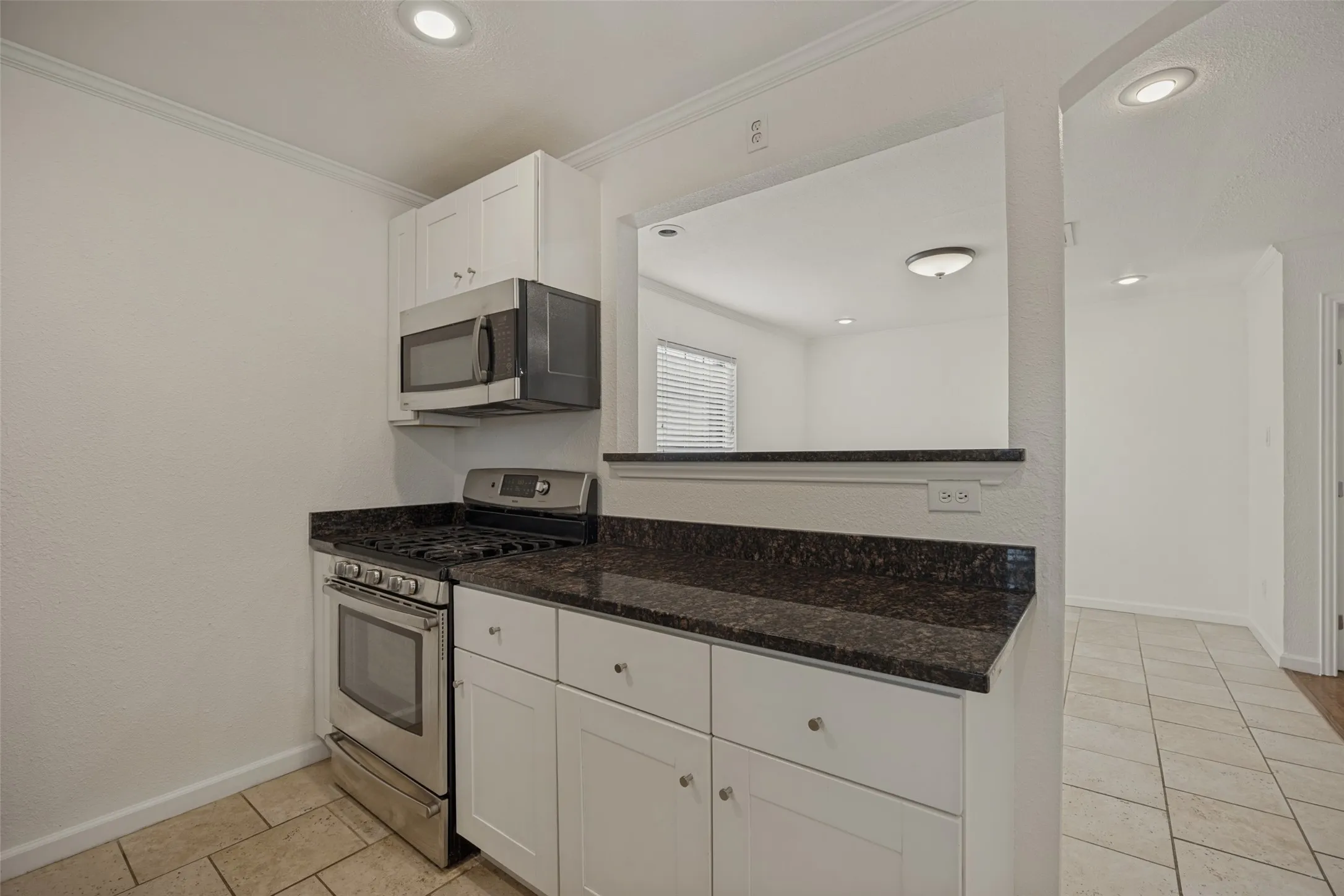 Stainless steel gas range and microwave, white cabinetry, dark stone countertops, and tile flooring