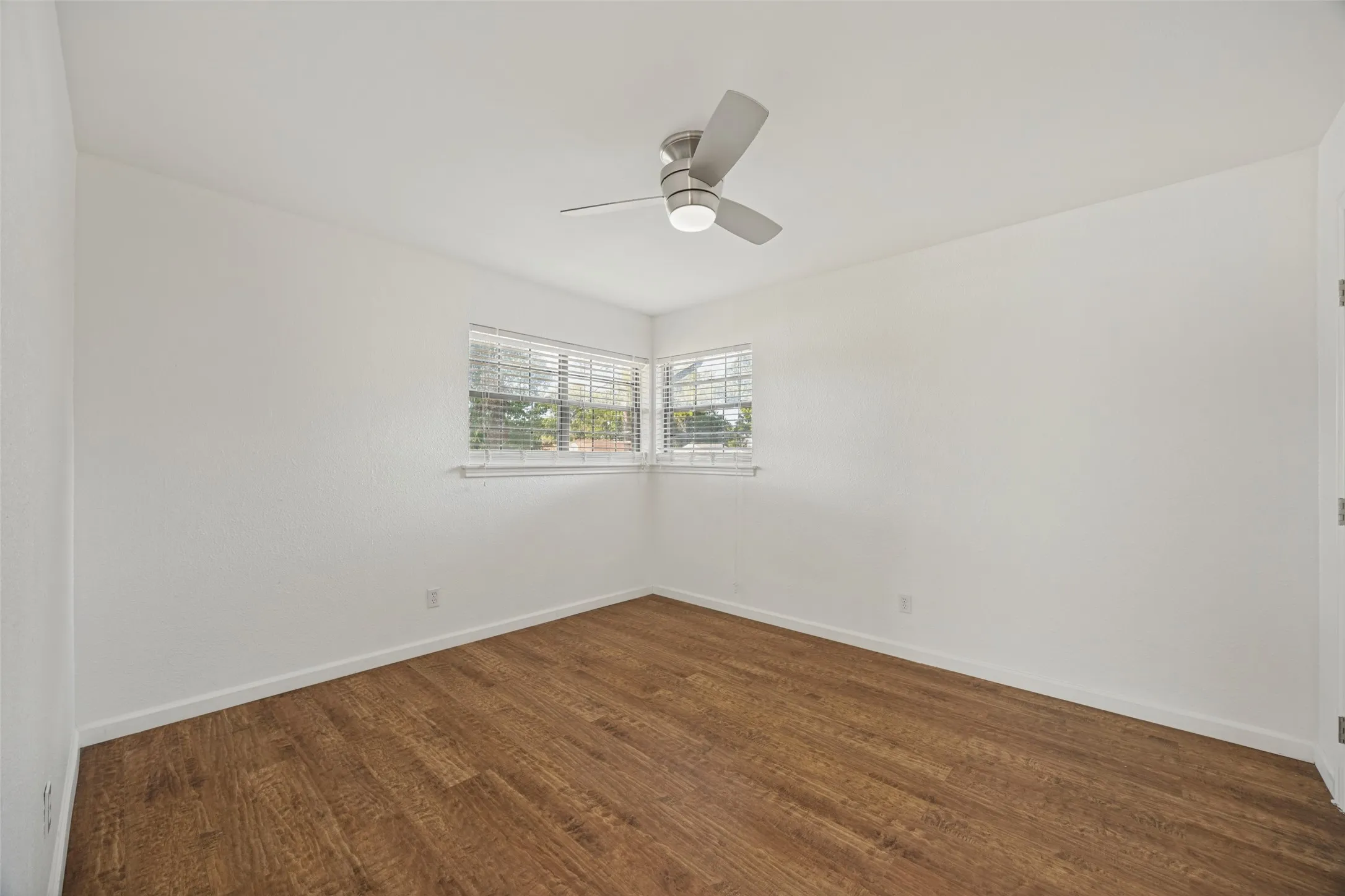 Wood-finish flooring, corner window with blinds, and a ceiling fan with integrated lighting