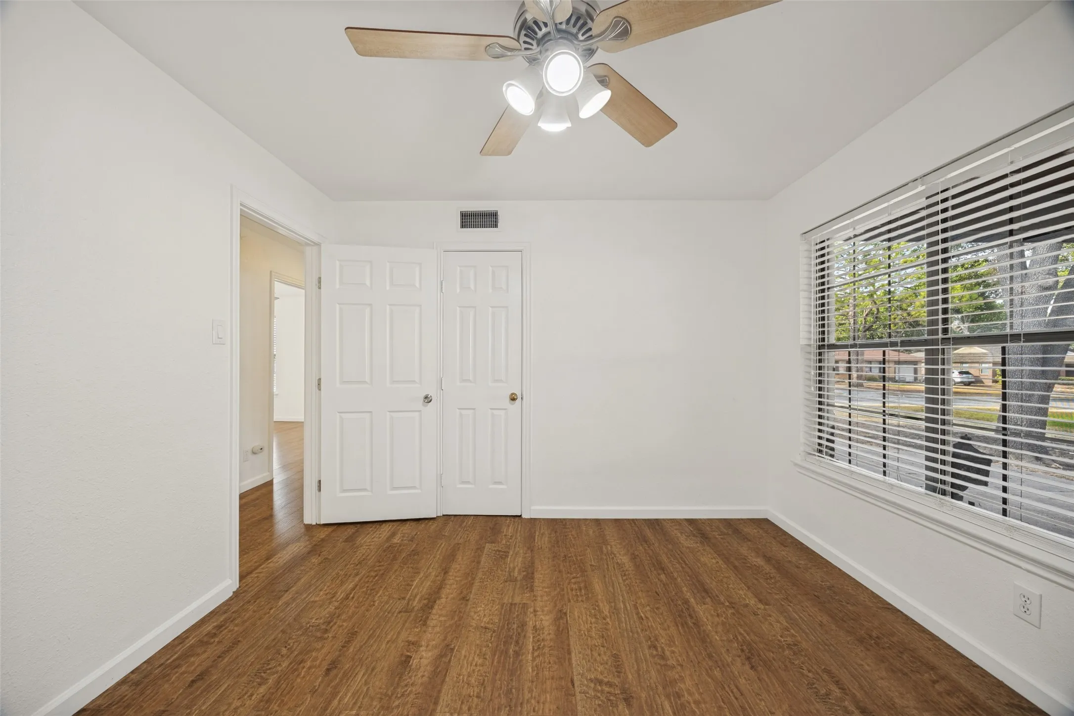 Wood-finish flooring, white walls, and a ceiling fan with integrated lighting