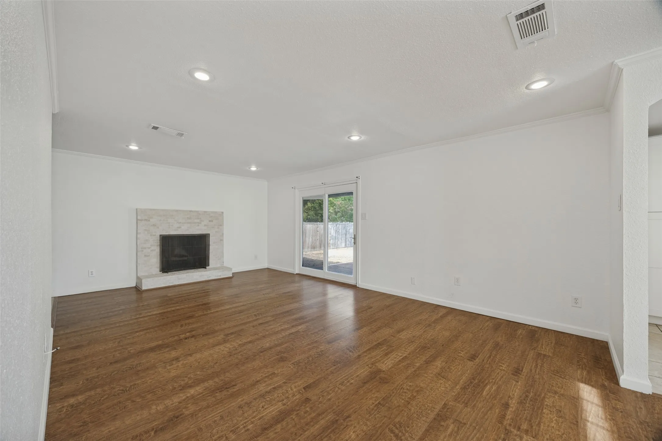 Wood-finish flooring throughout, white walls, recessed ceiling lighting, a fireplace with a stone surround, and a sliding glass door