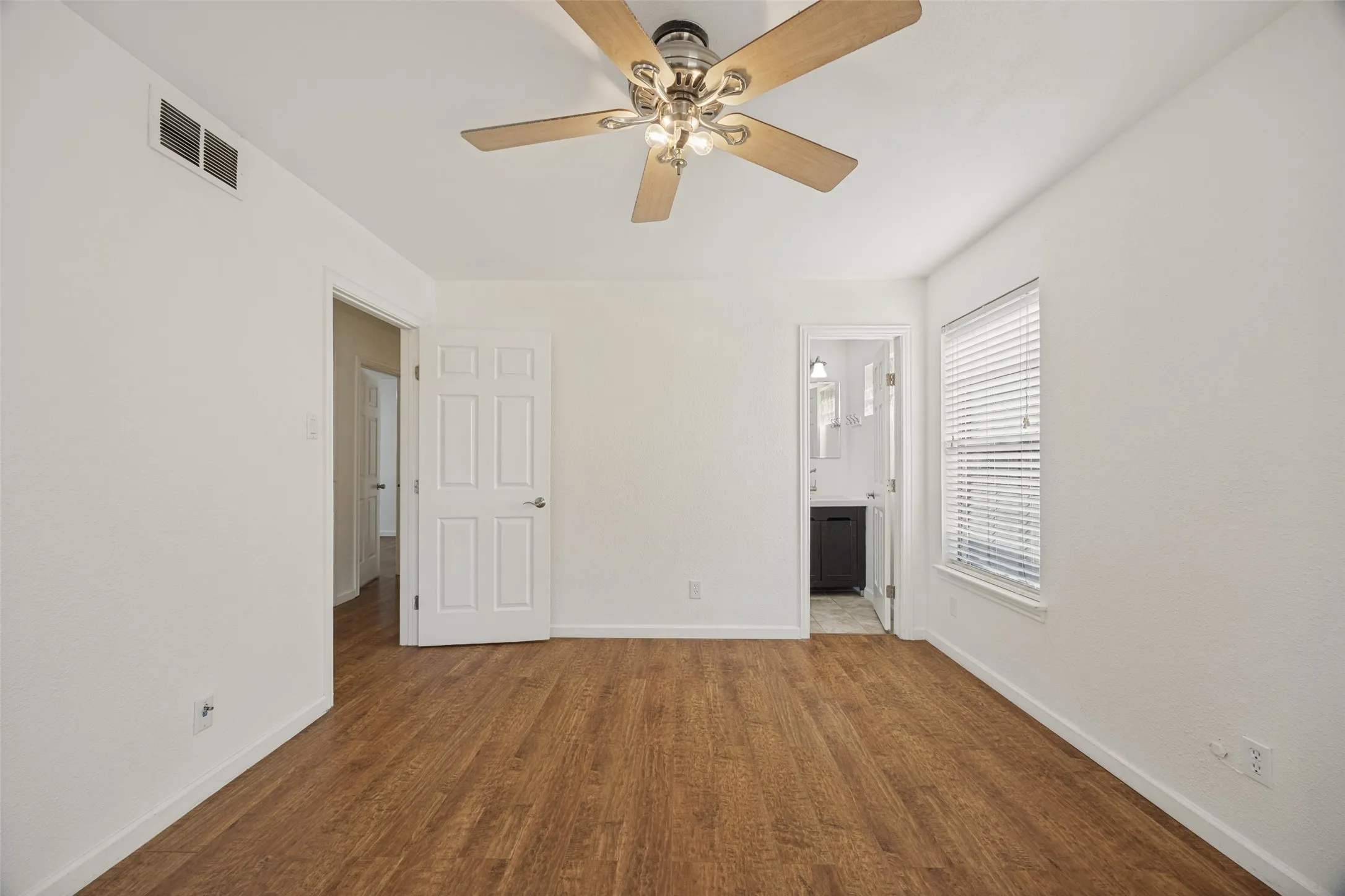 Wood-finish flooring, ceiling fan with light fixture, white interior walls, and window with blinds