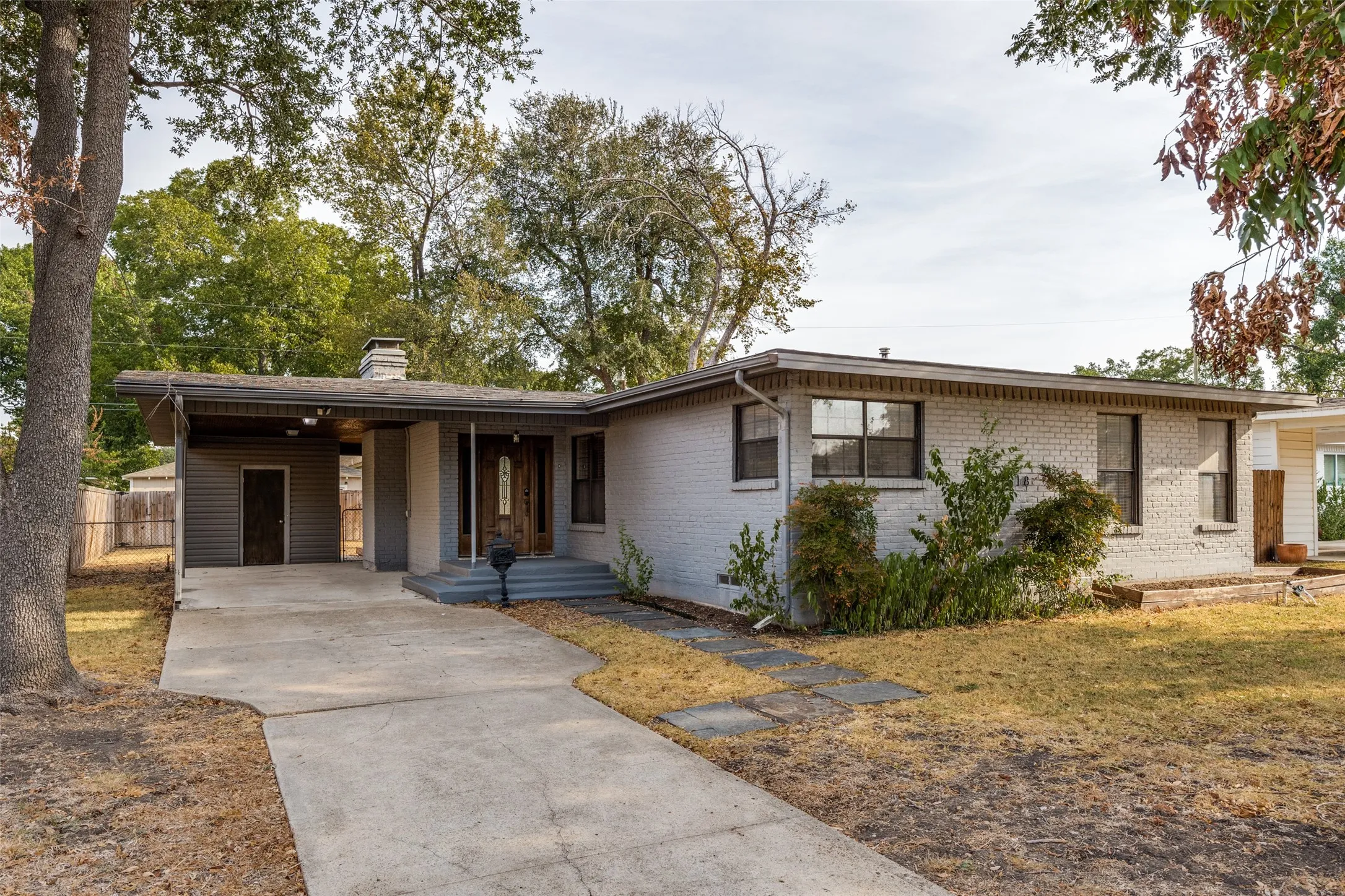 Painted brick exterior with a wood entry door, covered carport, and concrete driveway