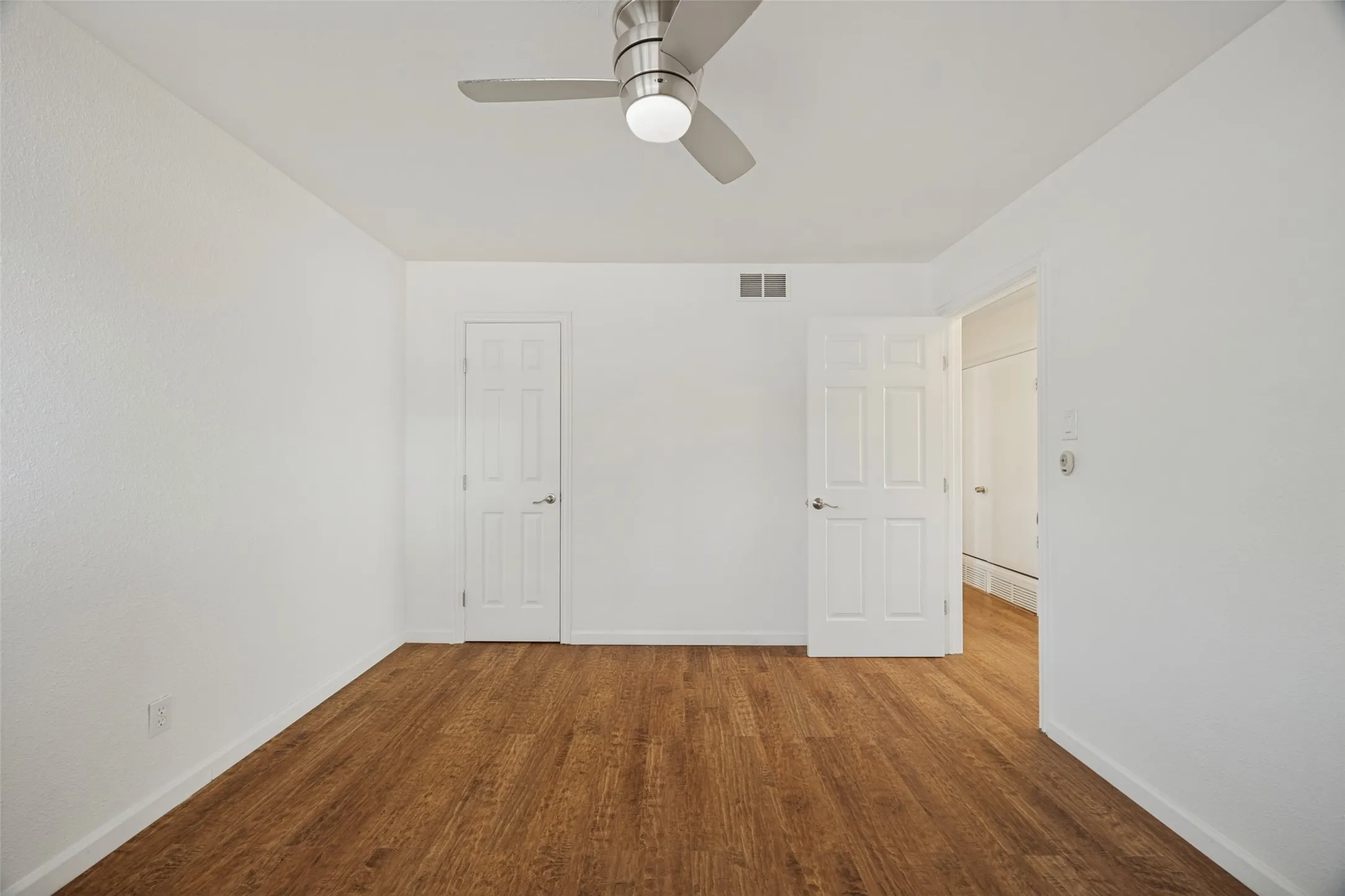 Wood-finish flooring, white paneled doors, ceiling fan with integrated lighting, and neutral wall tones