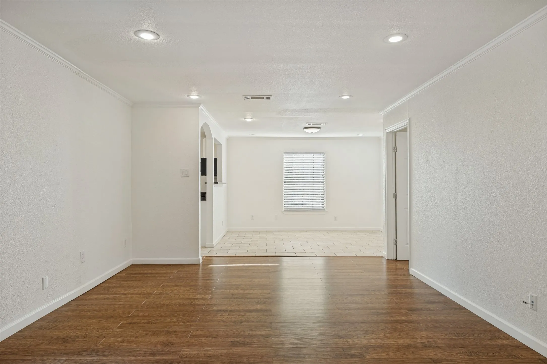 Wood-finish flooring, recessed lighting, crown molding, white painted walls, and an arched doorway