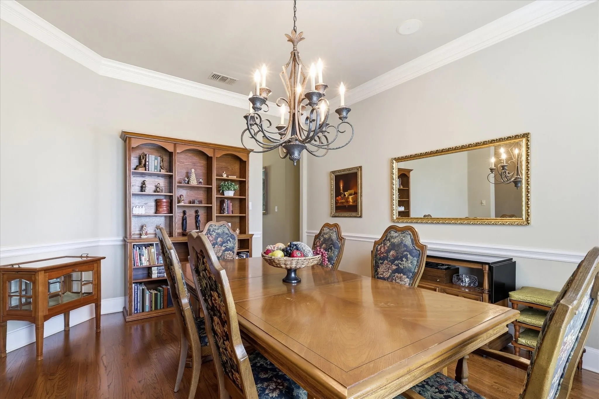 Crown molding, chair rail molding, wood-finish flooring, built-in shelving, and an ornate chandelier