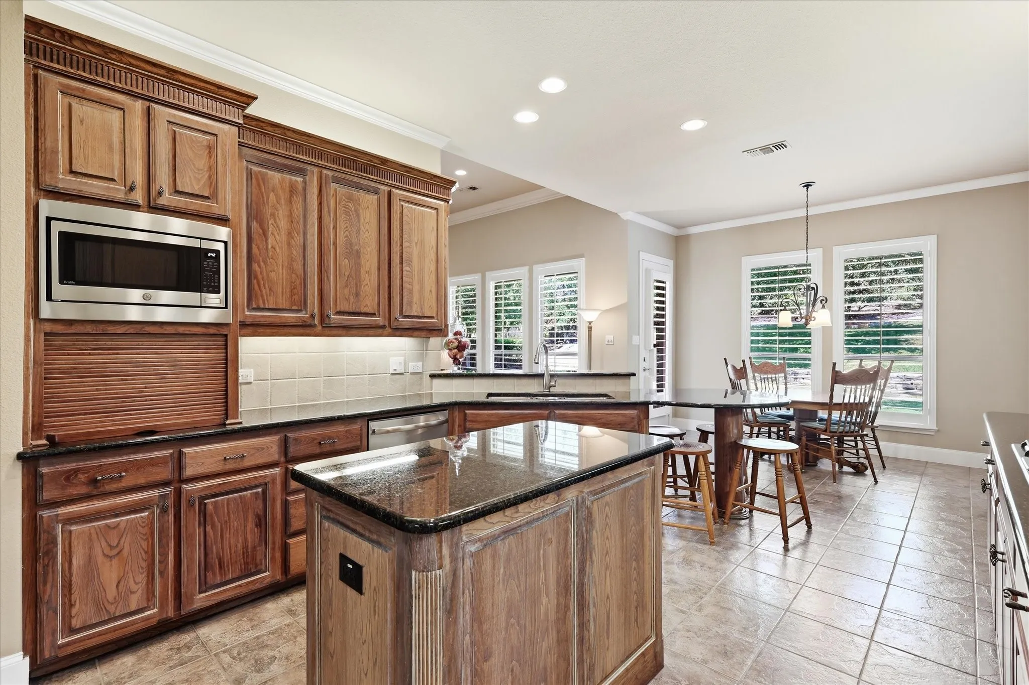 Wood cabinetry with stainless steel built-in microwave, dark countertops, and tile flooring