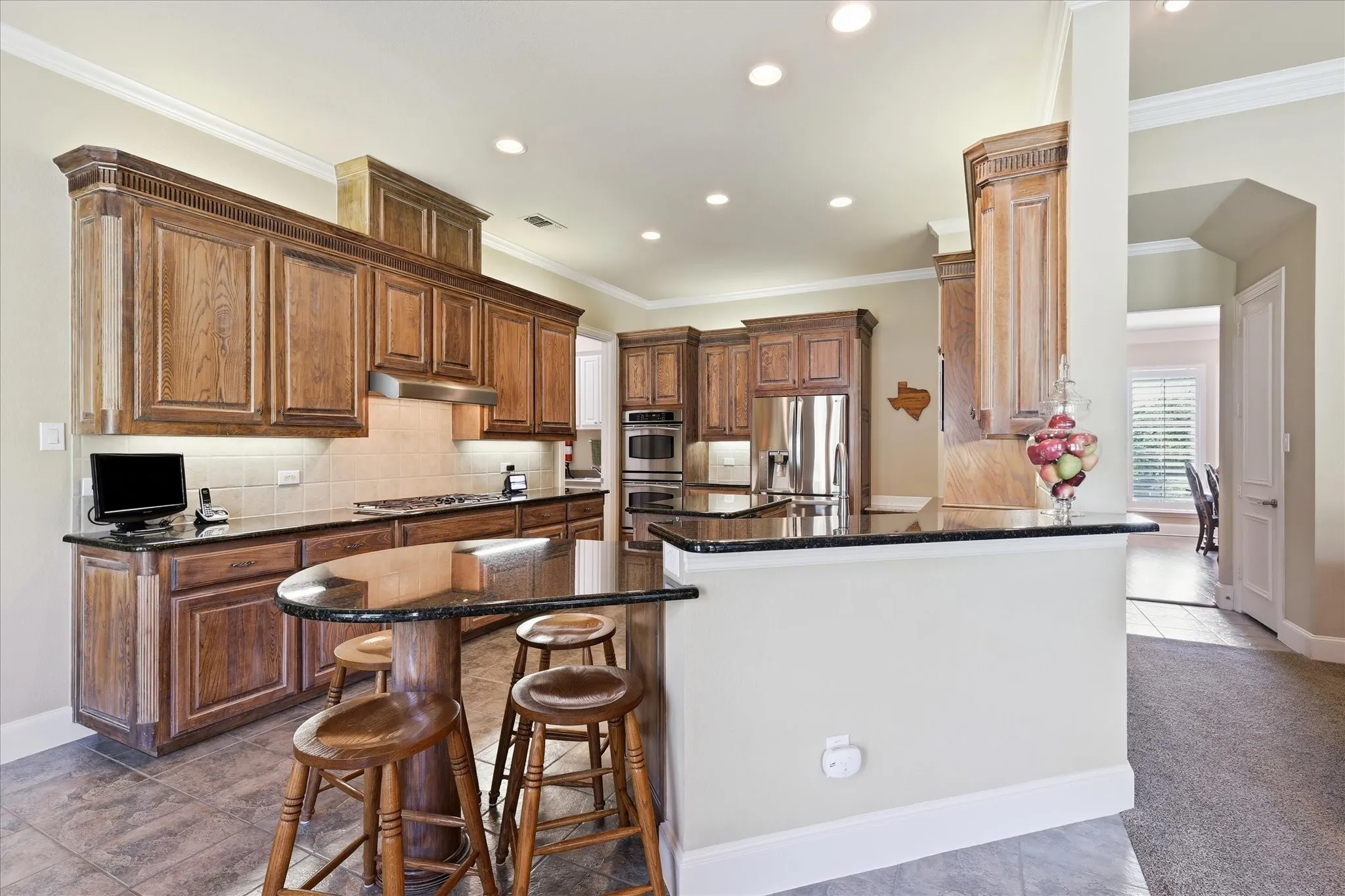 Gourmet kitchen with extensive wood cabinetry, dark countertops, built-in stainless steel appliances, a breakfast bar, and recessed lighting