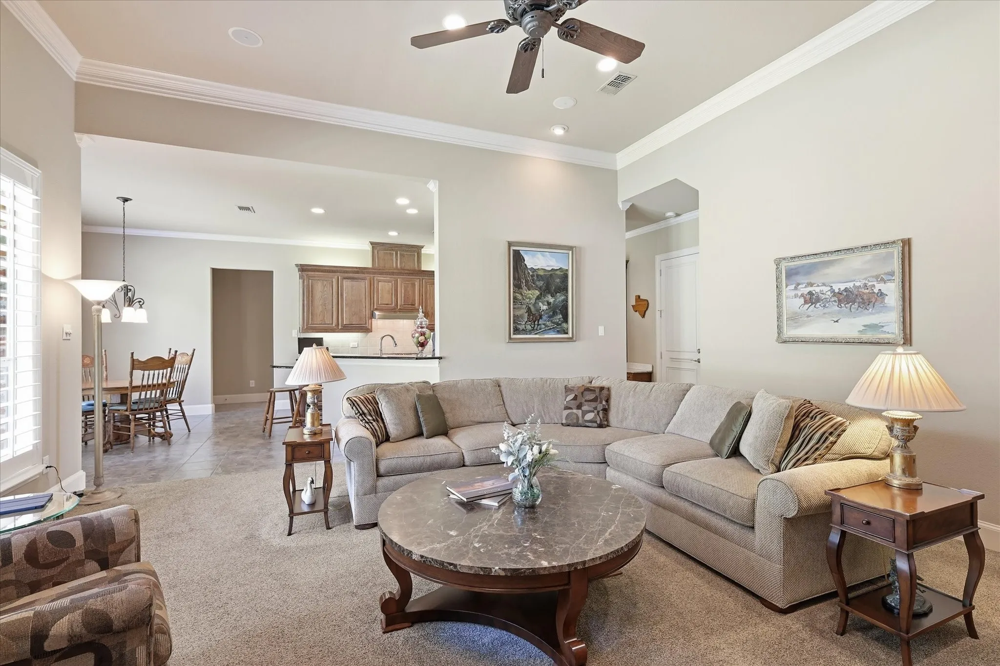 Spacious living area featuring carpet flooring, crown molding, and a ceiling fan