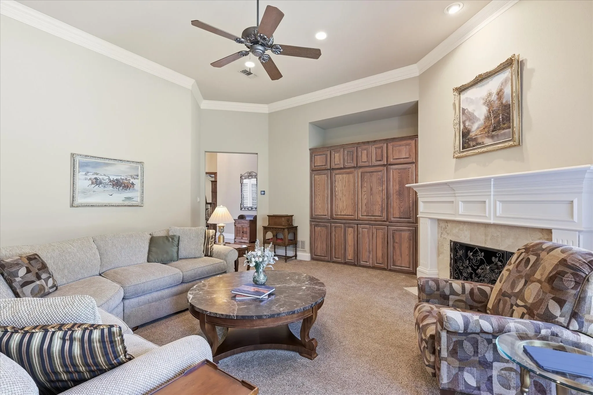 Living area featuring a fireplace with a decorative mantel, built-in wood cabinetry, recessed lighting, and a ceiling fan