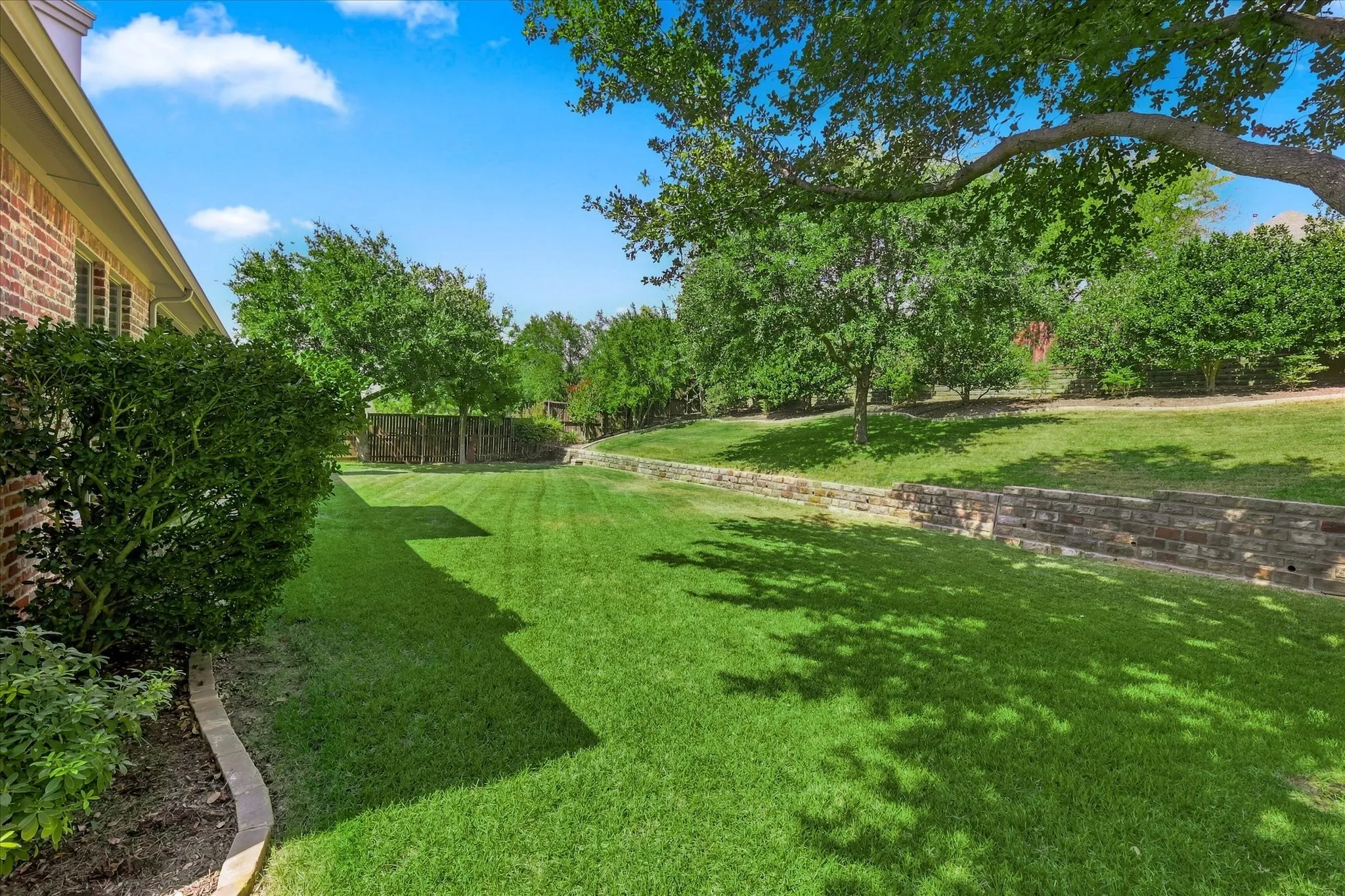 Expansive green lawn with mature trees, a stone retaining wall, and defined landscaping borders