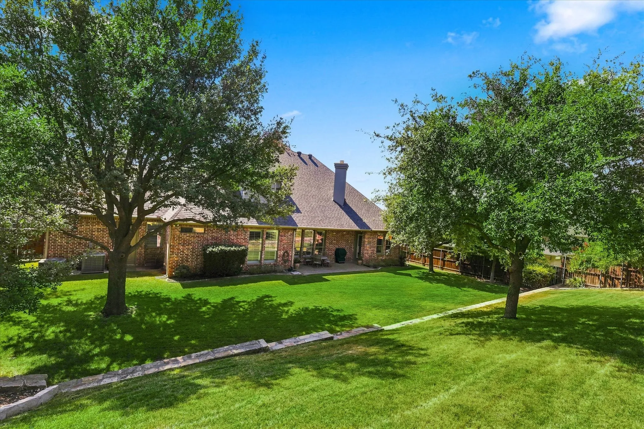Expansive green lawn with mature trees, brick exterior, and a spacious patio area
