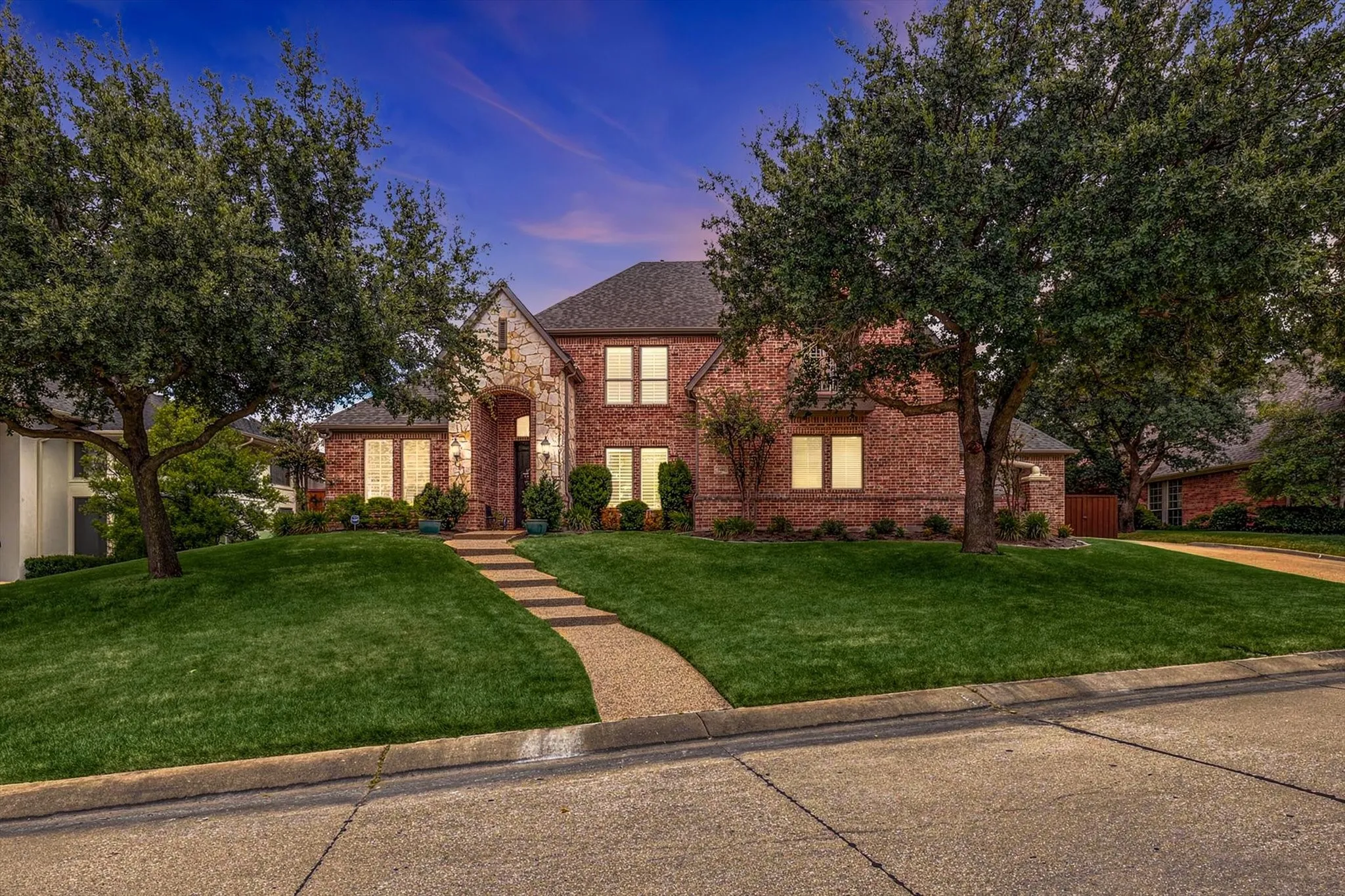 Brick exterior with stone accents, mature trees, a stepped pathway, and a well-maintained lawn