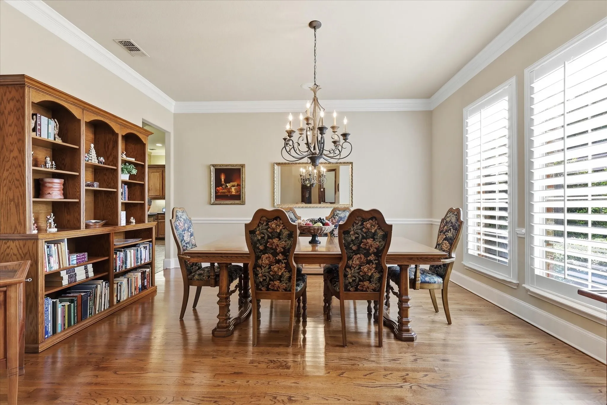 Hardwood flooring, crown molding, built-in shelving, chandelier, and white plantation shutters