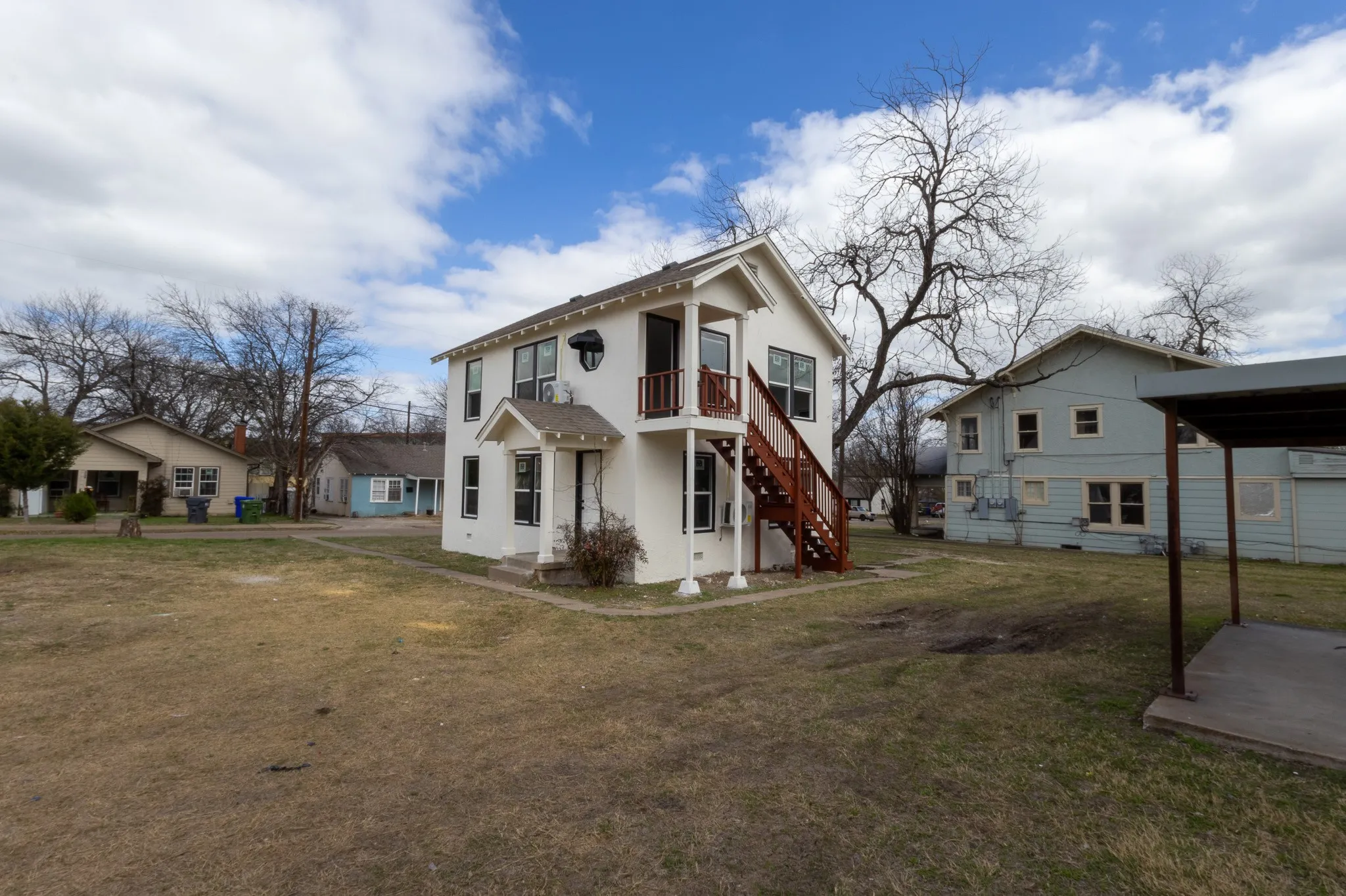 Two-story stucco exterior with a covered entry, upper-level balcony, and exterior staircase