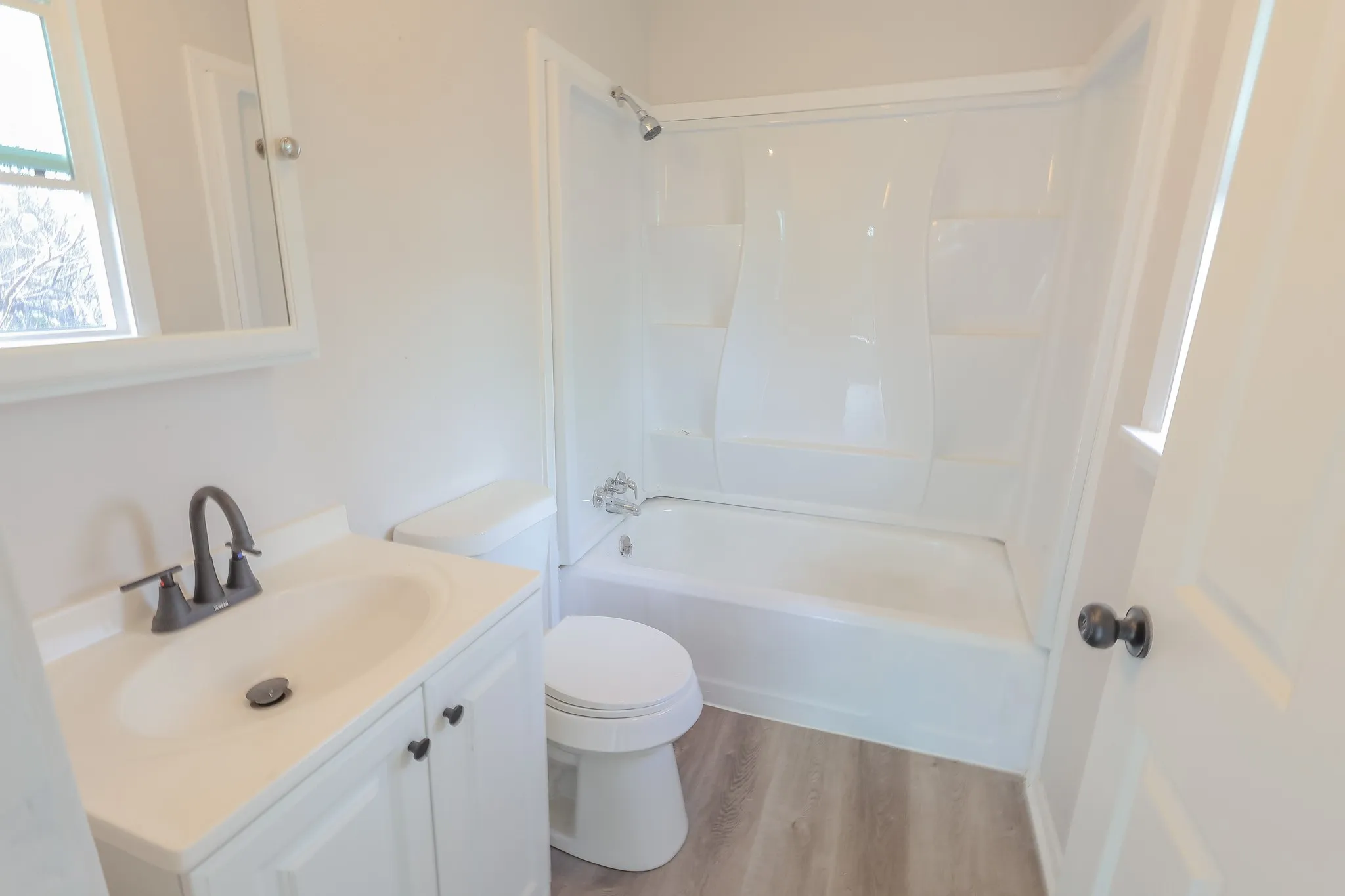 Contemporary bathroom featuring a white vanity with integrated sink, dark bronze-finish faucet, and a white bathtub with shower